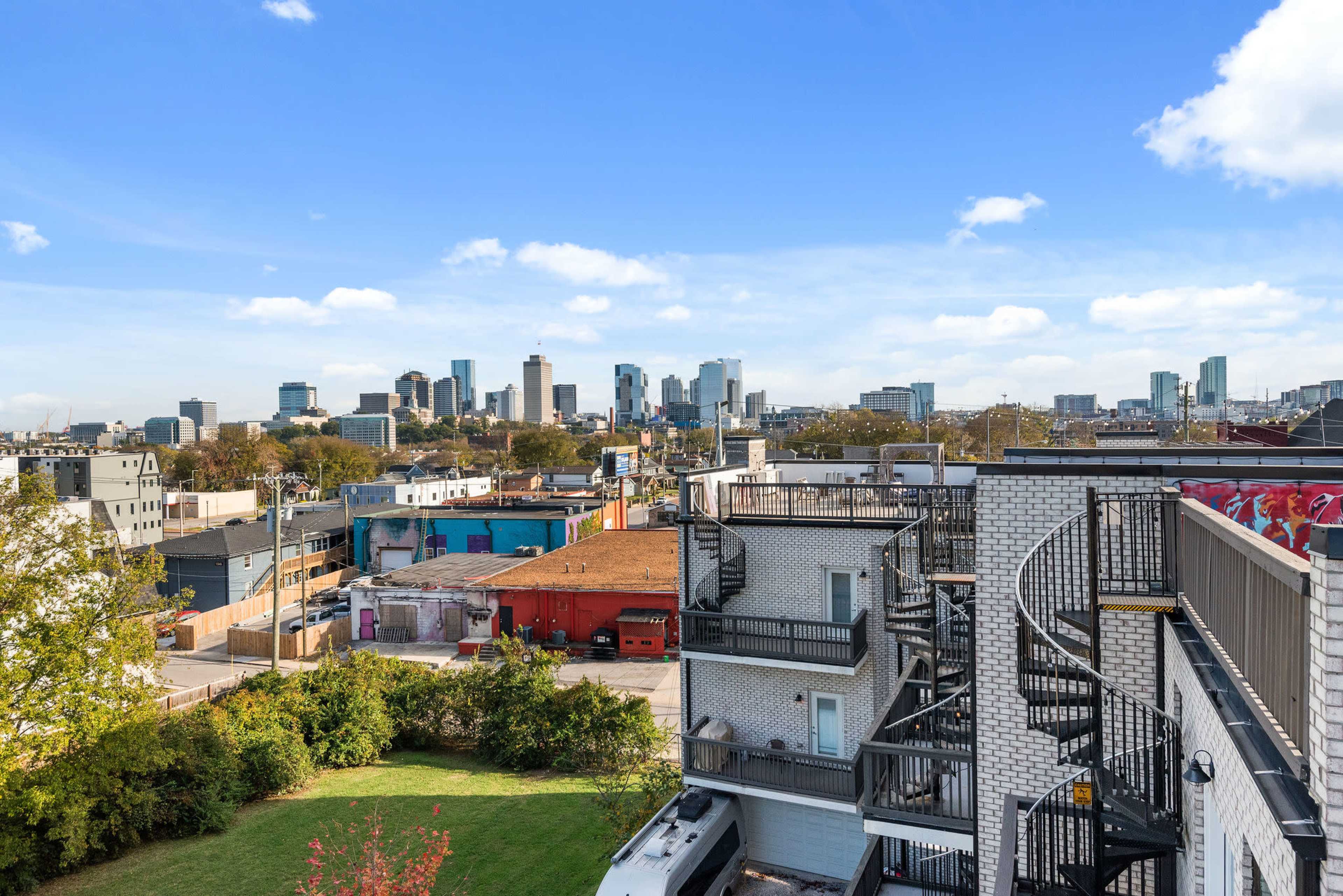 The image shows a city skyline with modern high-rise buildings in the background and a neighborhood featuring low-rise structures and greenery in the foreground.