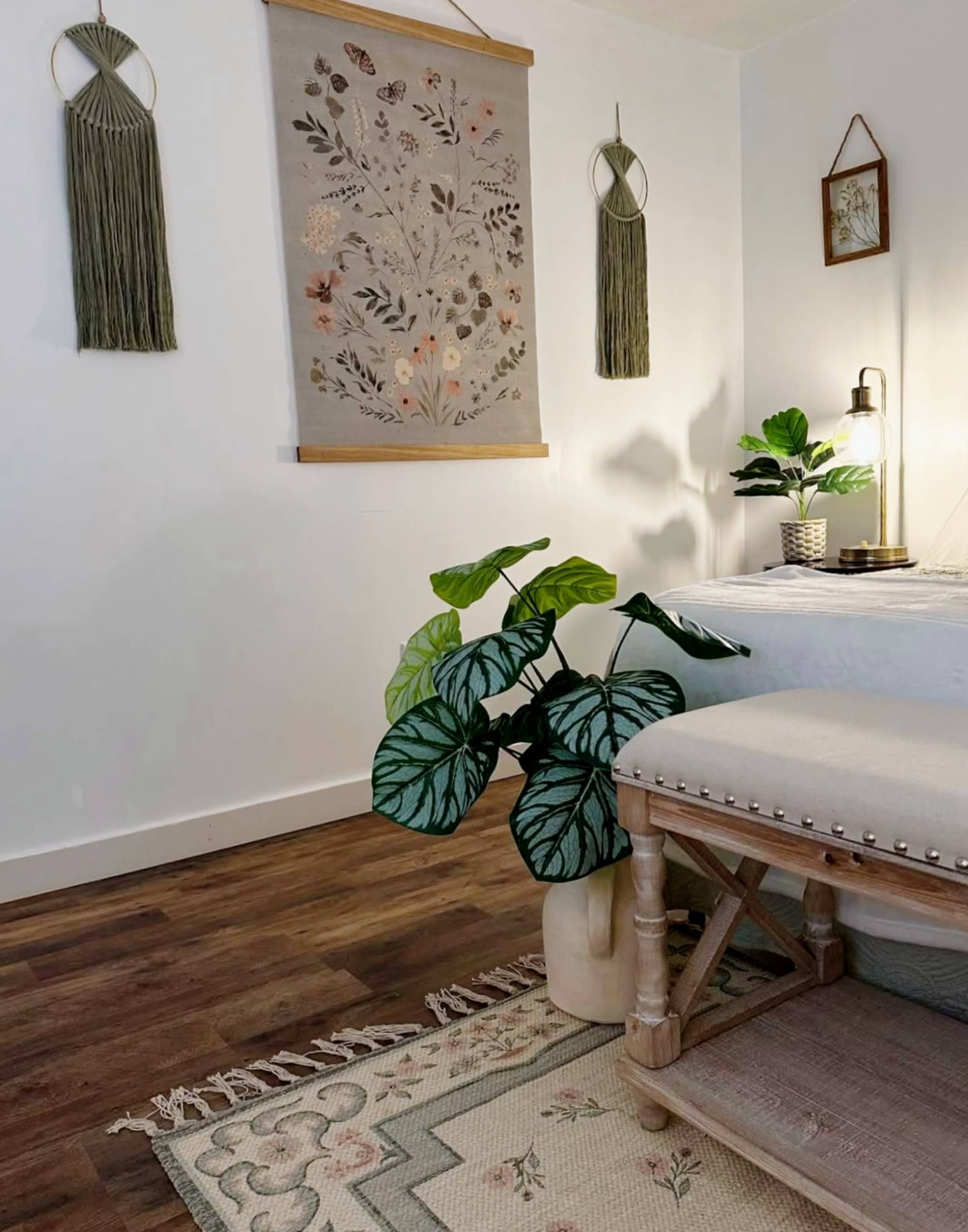 The image shows a cozy indoor space featuring a potted plant, a wooden stool with a woven rug underneath, and a decorative wall hanging.