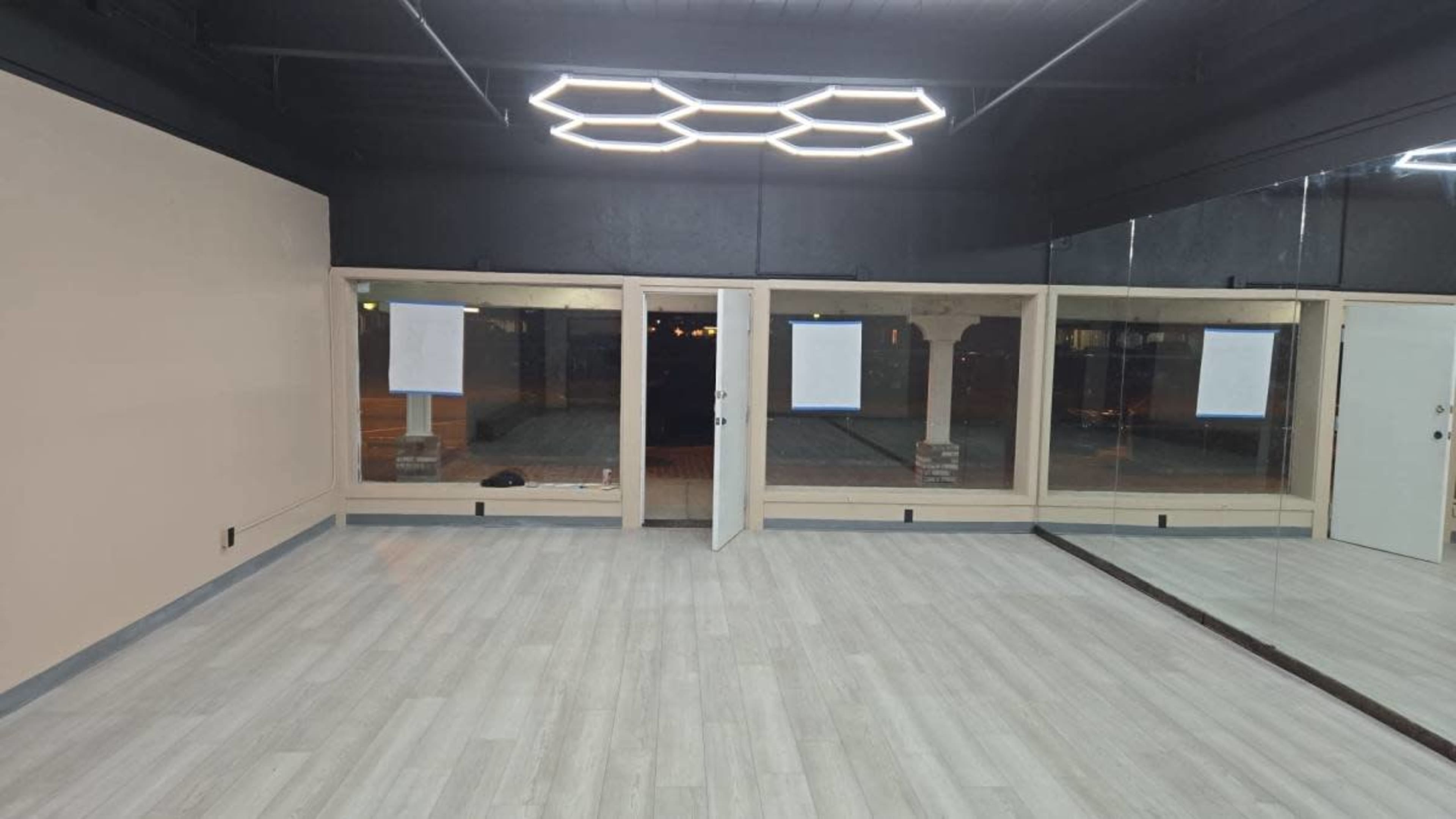 The image shows an empty interior room with light-colored flooring and large windows featuring paper coverings.