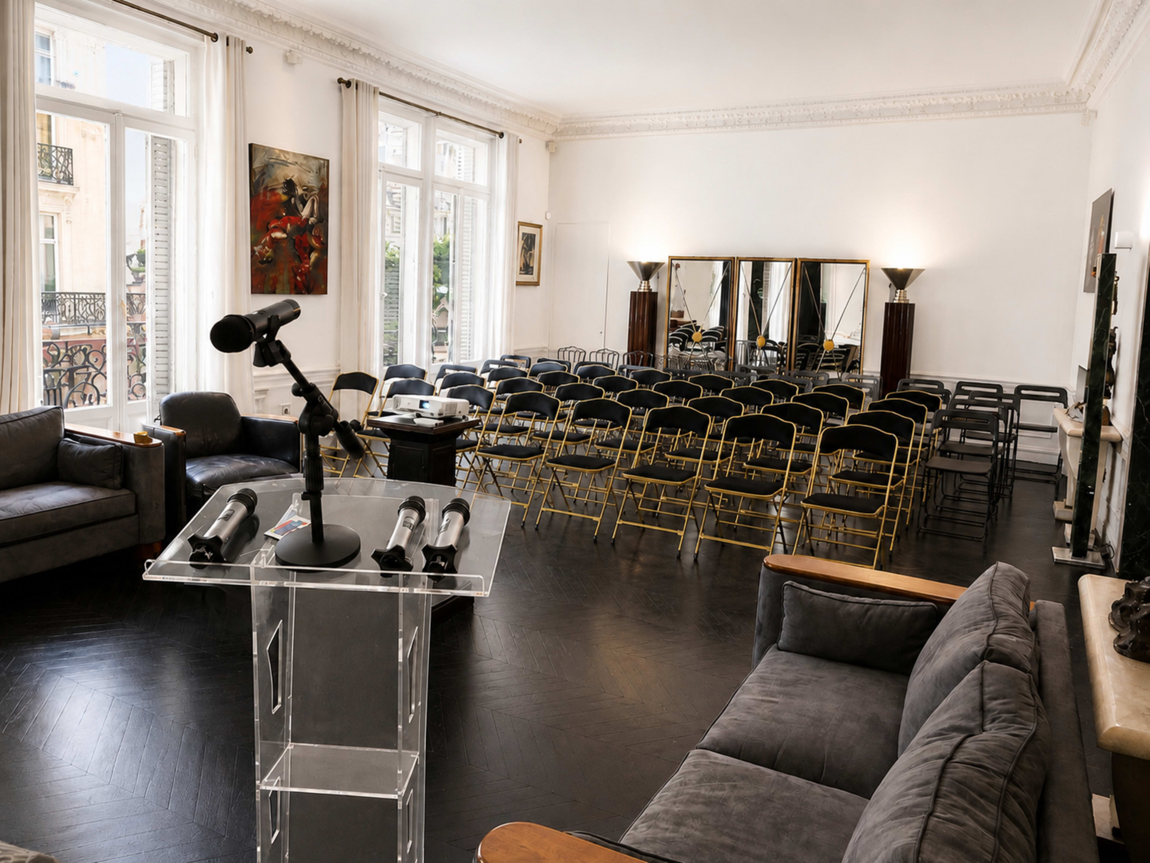 A spacious room is set up for an event, featuring rows of chairs, a podium with microphones, and large mirrors on one wall.