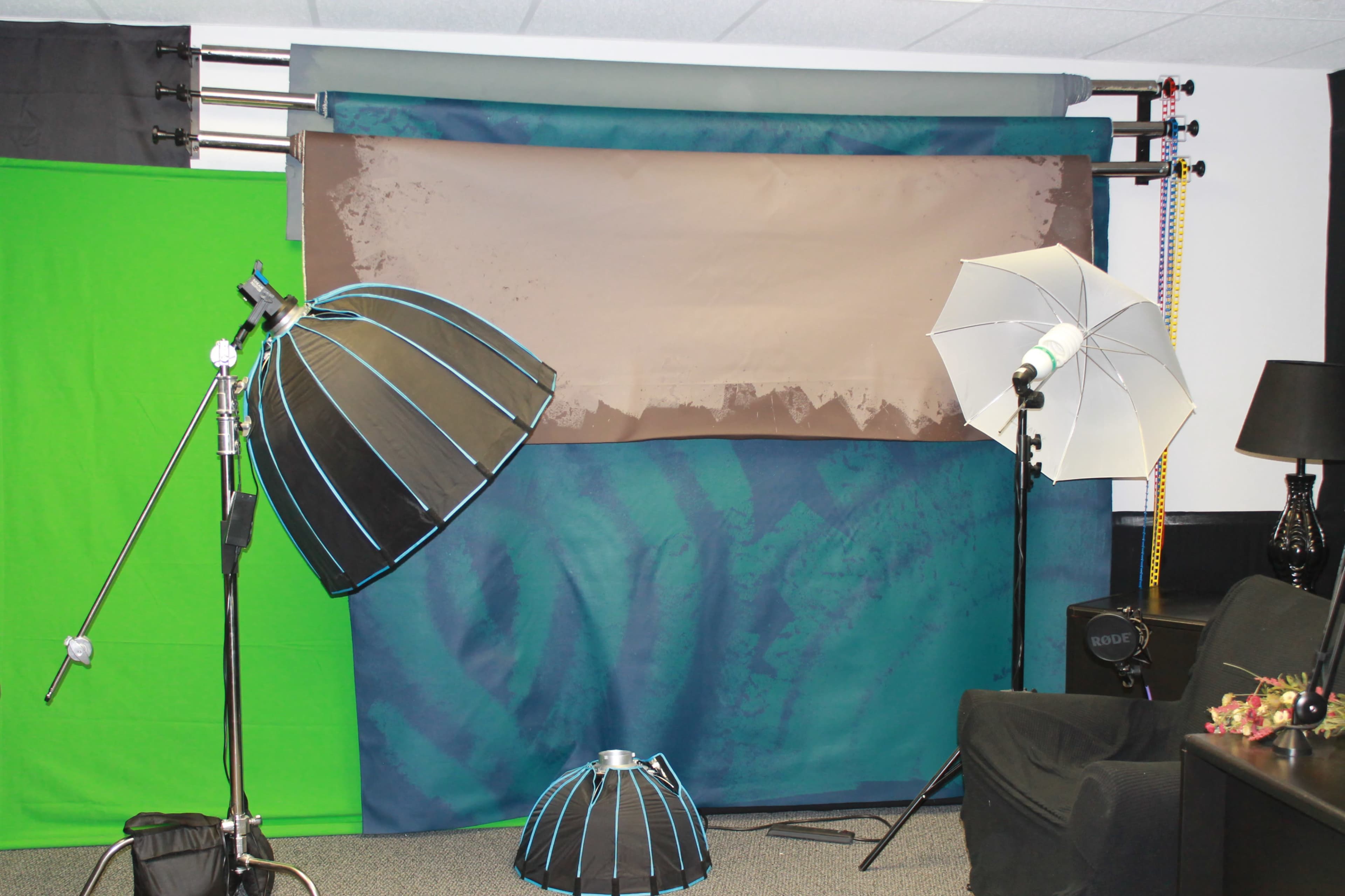 A photography studio setup with various backdrops, lighting equipment, and reflectors arranged in the space.