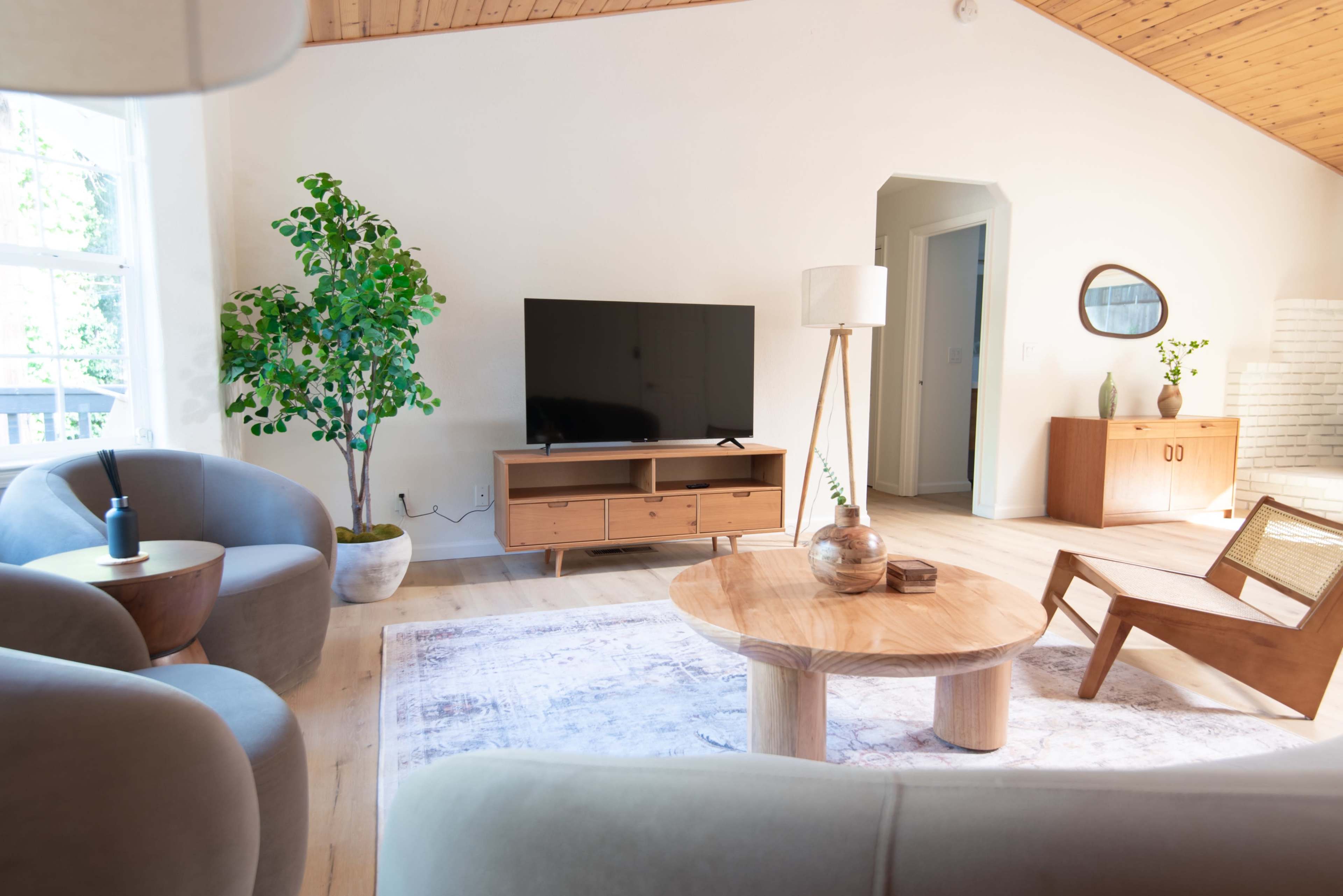A modern living room with two armchairs, a round coffee table, a television unit, and cabinetry, surrounded by natural light from large windows.