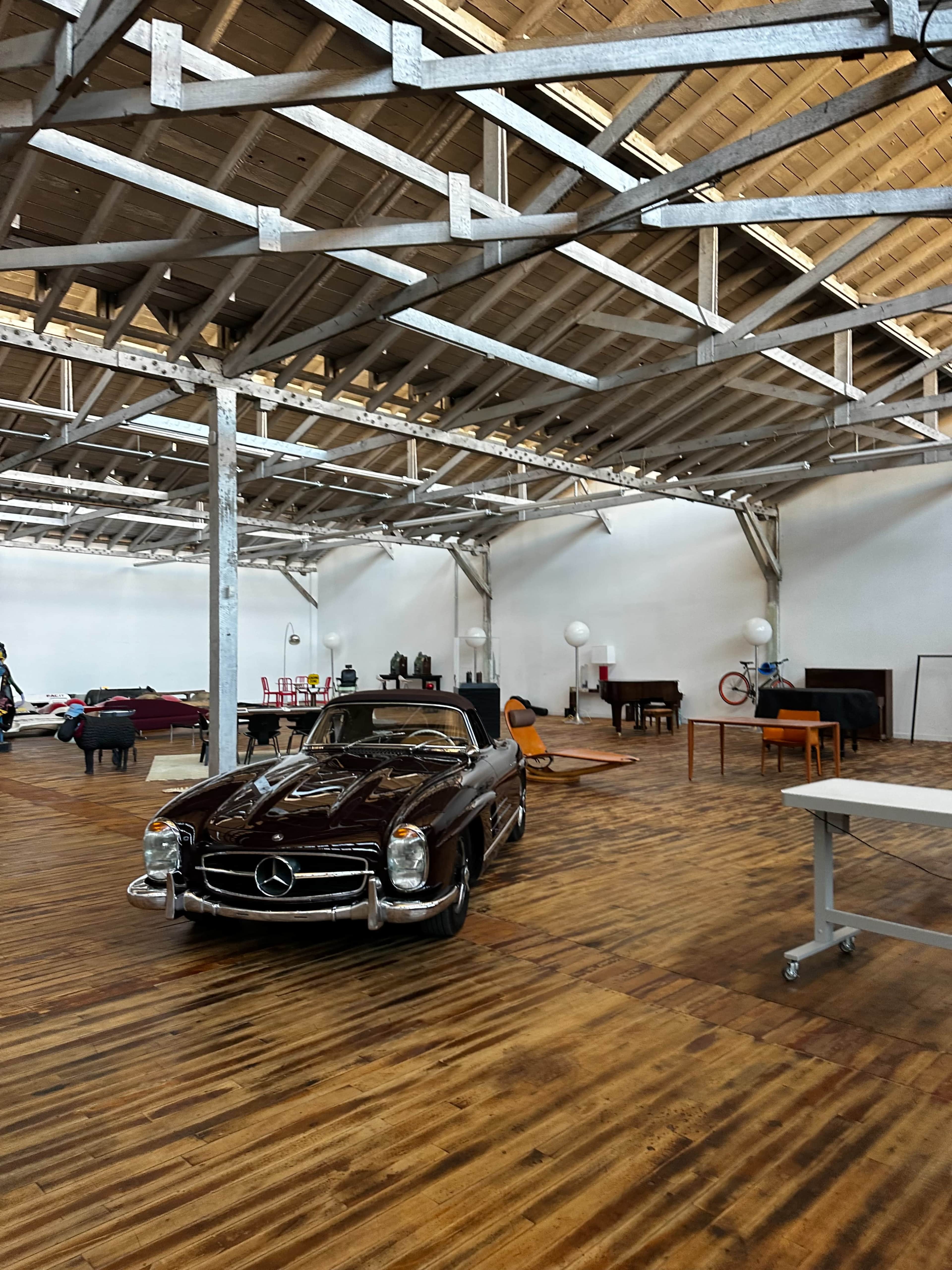 A classic Mercedes-Benz sports car is parked in a spacious, modern interior with wooden flooring and exposed beams.