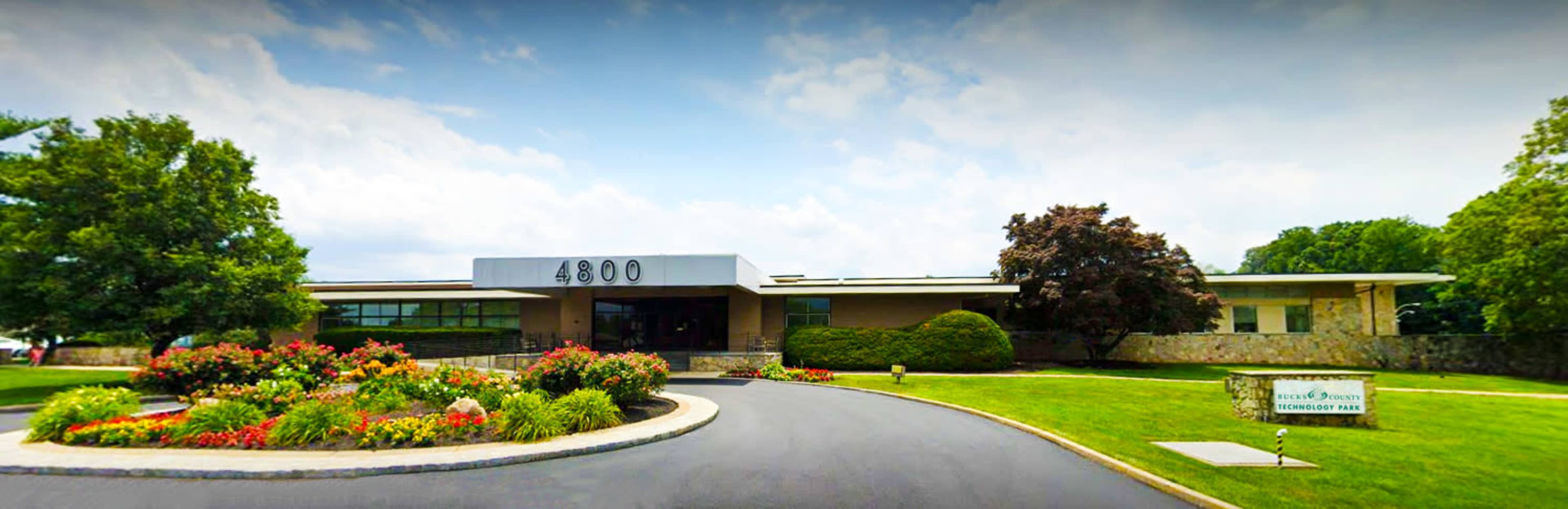 A modern single-story building with the number "4800" prominently displayed above the entrance, surrounded by landscaped gardens and a circular driveway.