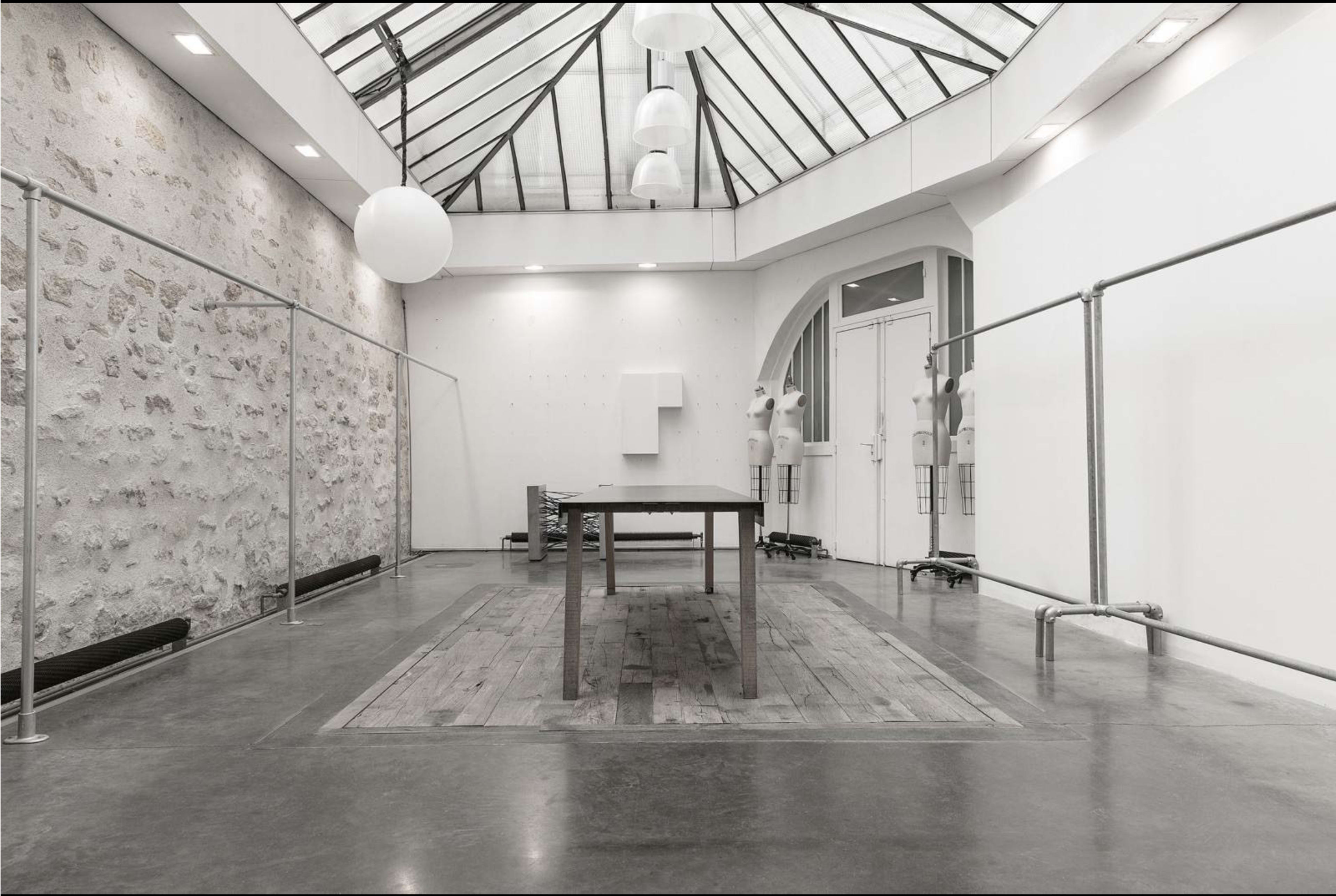 A spacious, well-lit interior with a wooden table in the center, surrounded by a minimalist design featuring a glass ceiling and stone walls.
