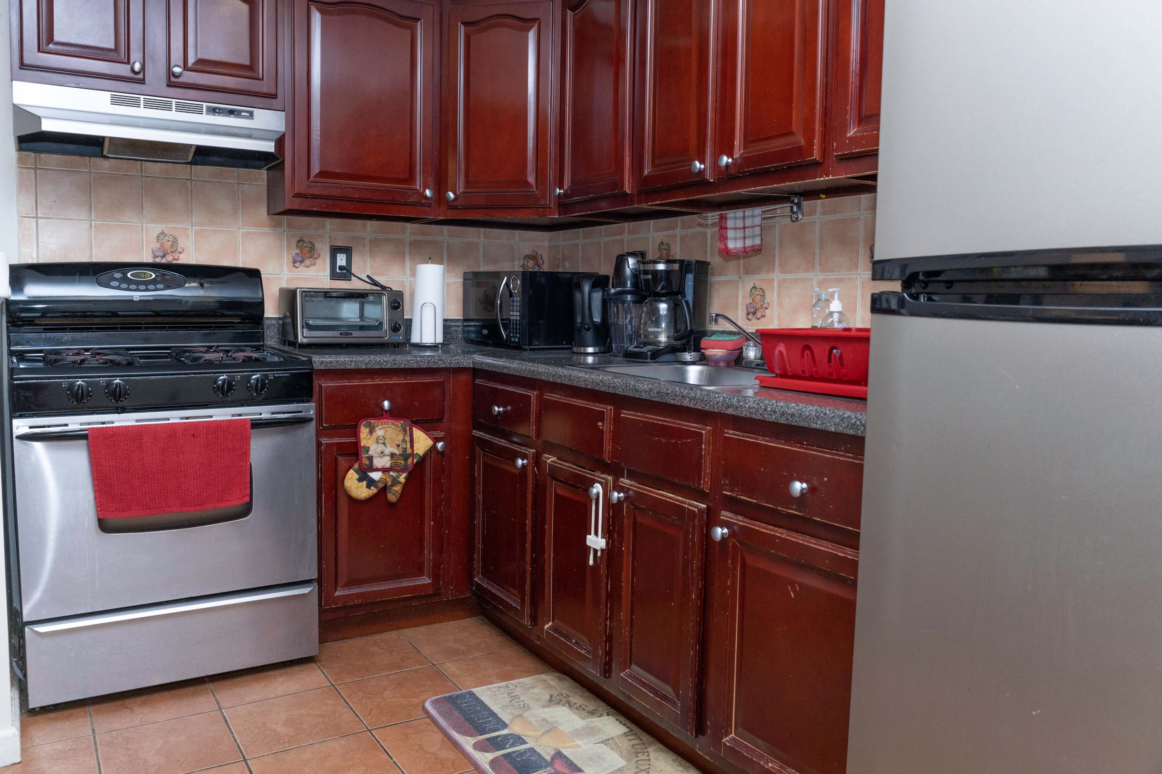 A kitchen with dark wooden cabinets, a stainless steel stove and refrigerator, and a countertop with various appliances and utensils.