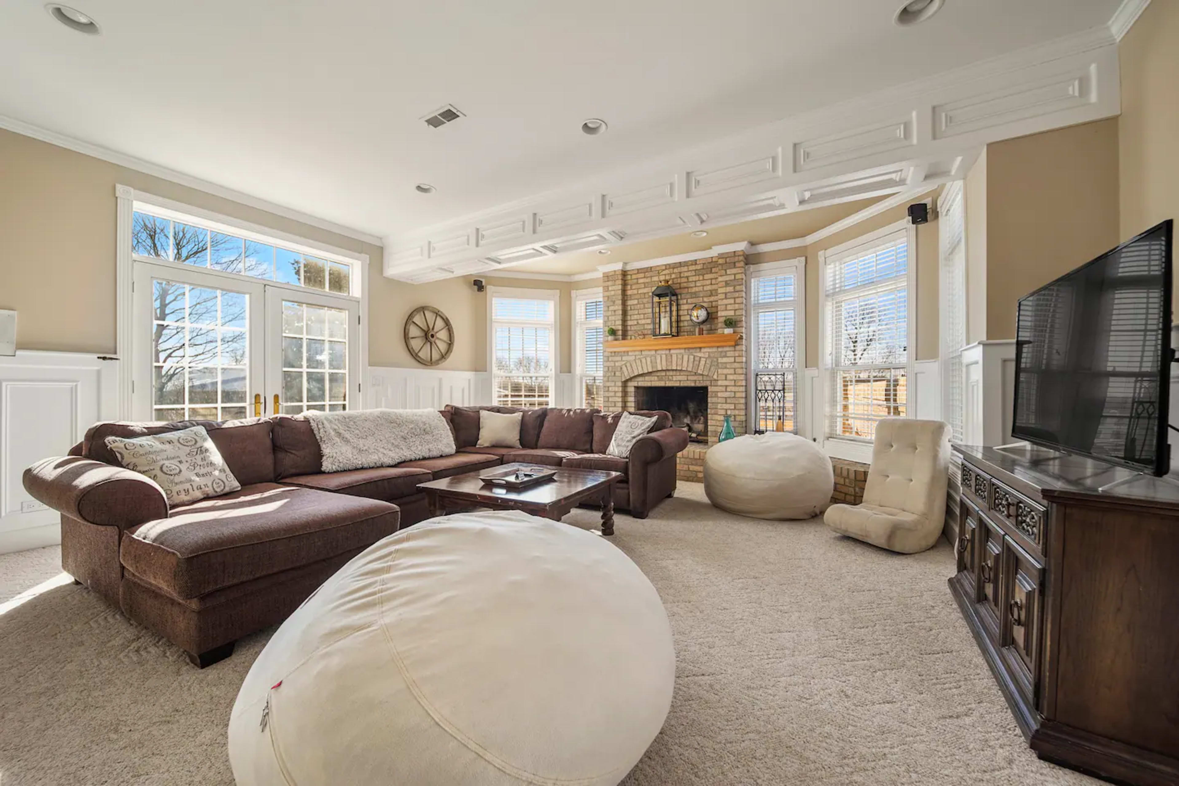A spacious living room features a large sectional sofa, two bean bags, a coffee table, and a fireplace surrounded by windows.