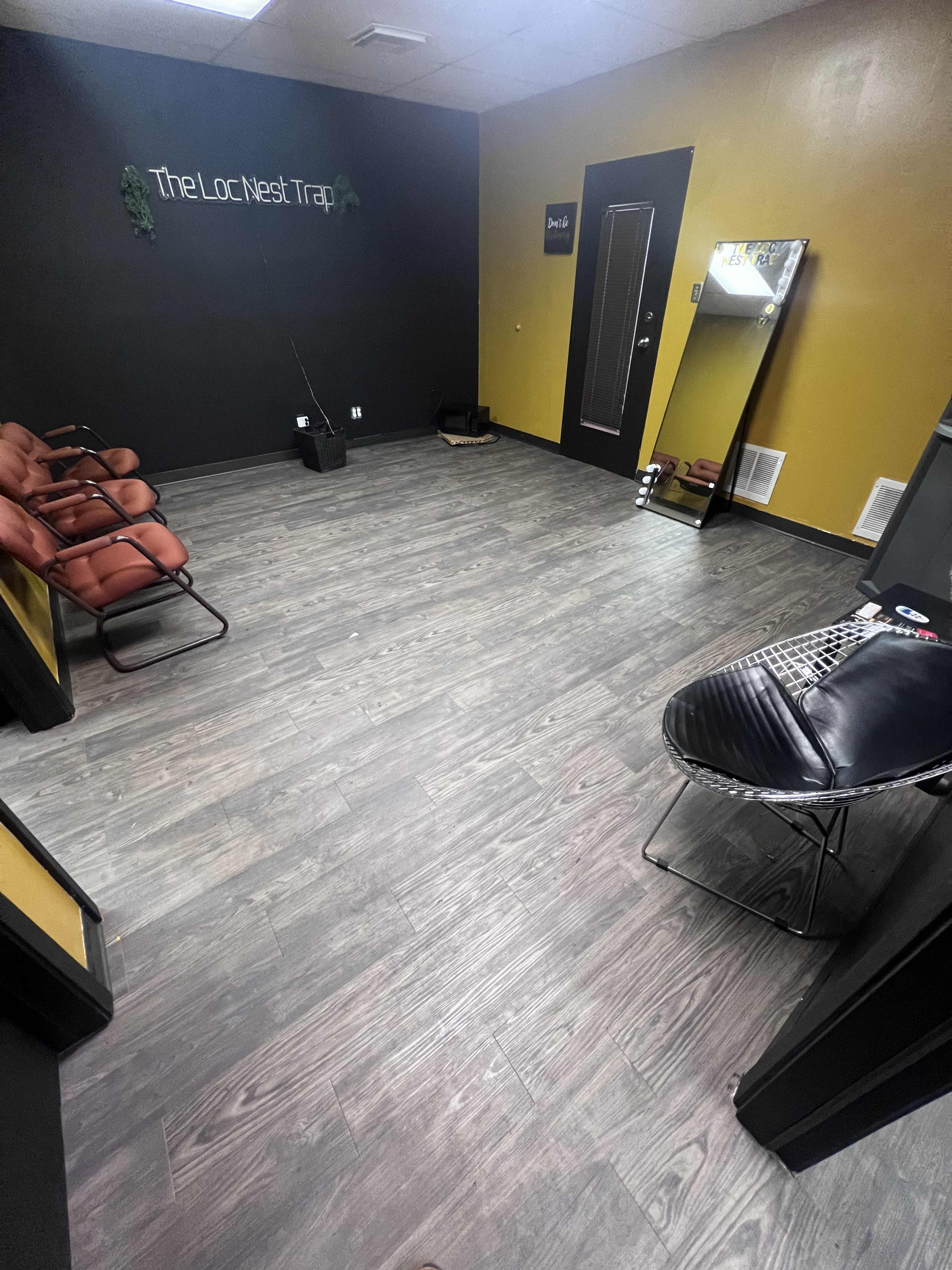 The image shows a sparsely furnished room with a black and yellow color scheme, featuring several chairs, a mirror, and a stylist's chair.