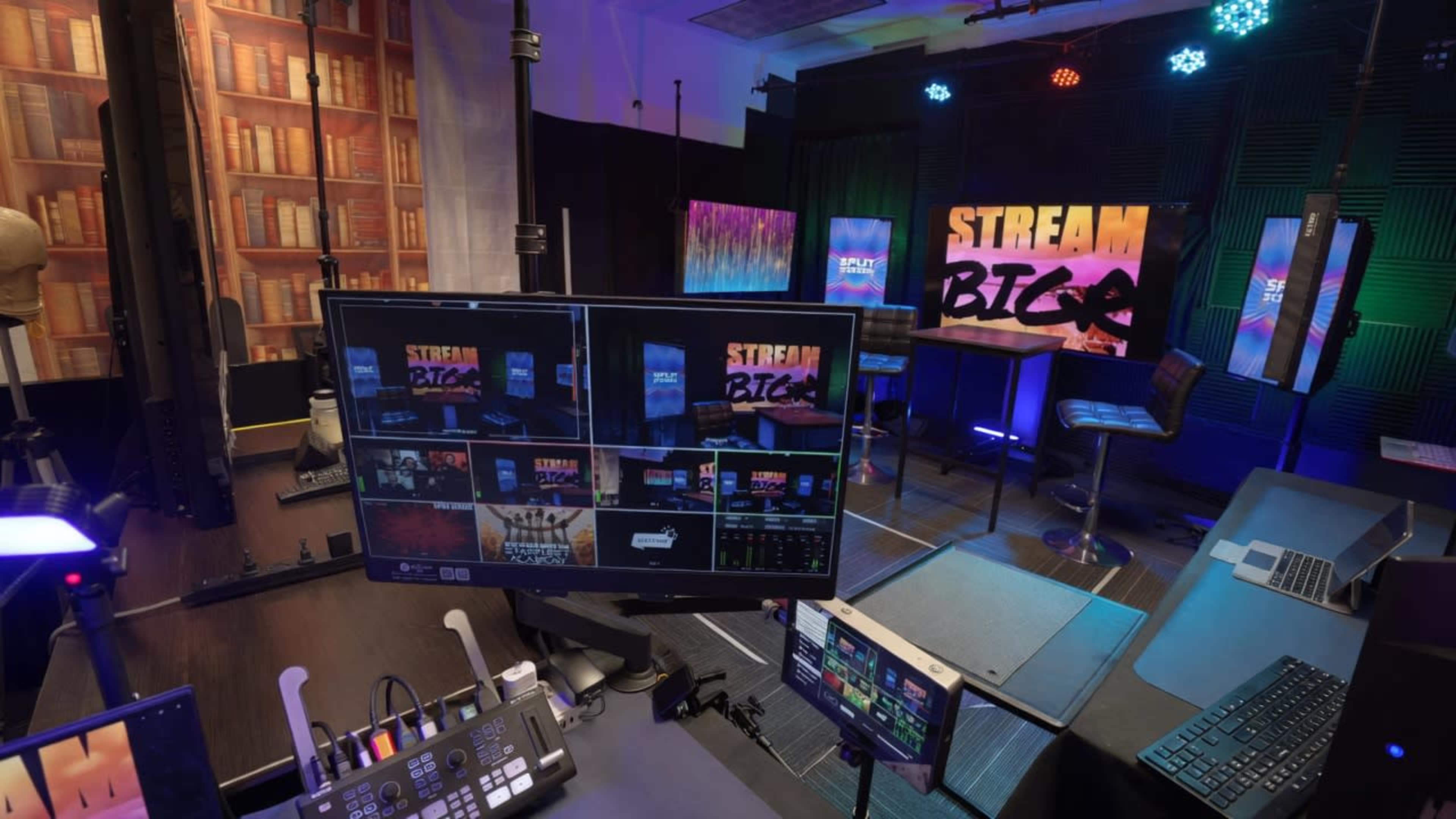 The image shows a modern streaming studio equipped with multiple monitors, colorful lighting, and a backdrop featuring text that reads "STREAM BTL."