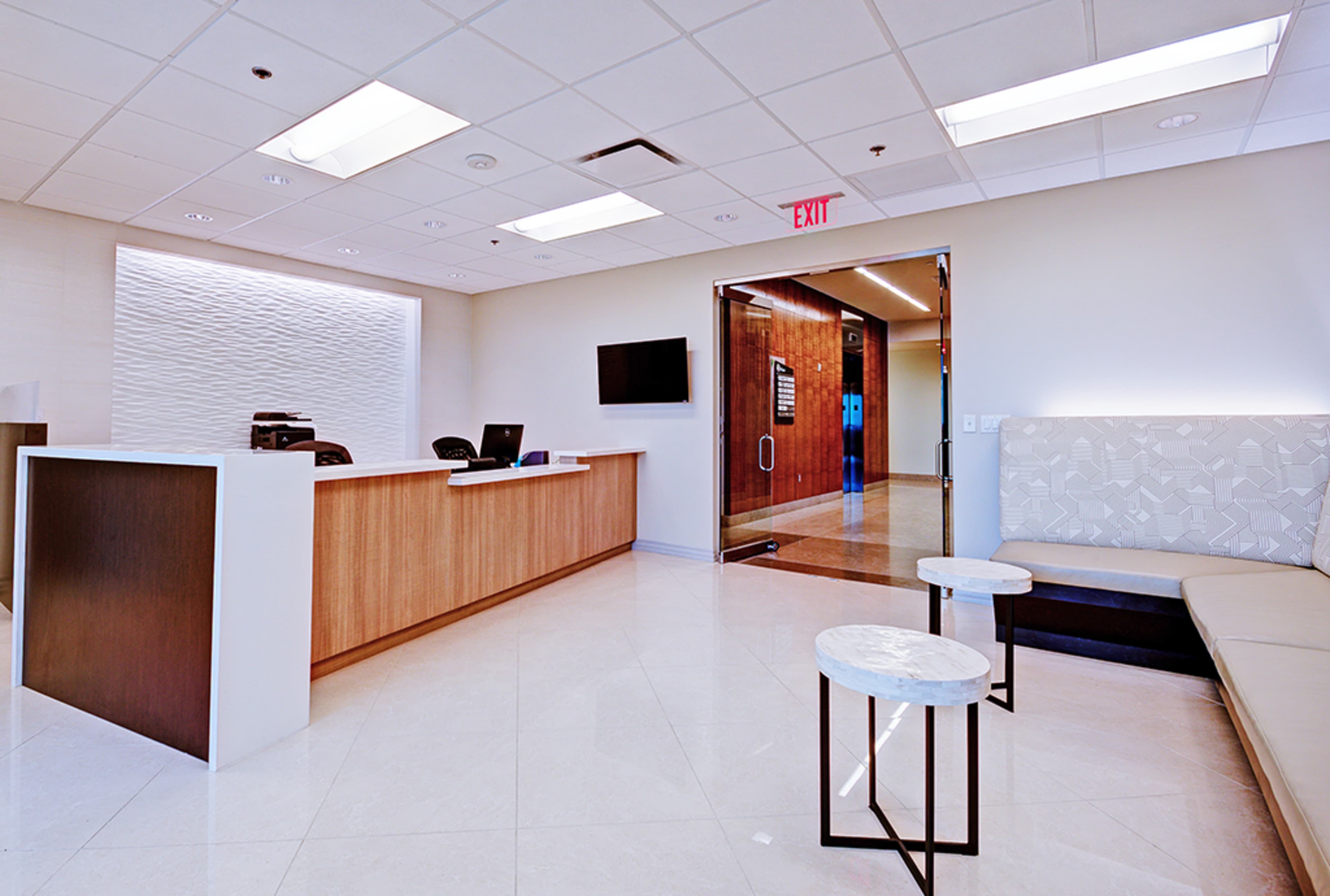 A modern reception area with a wooden front desk, minimalist seating, and a glass entrance door.