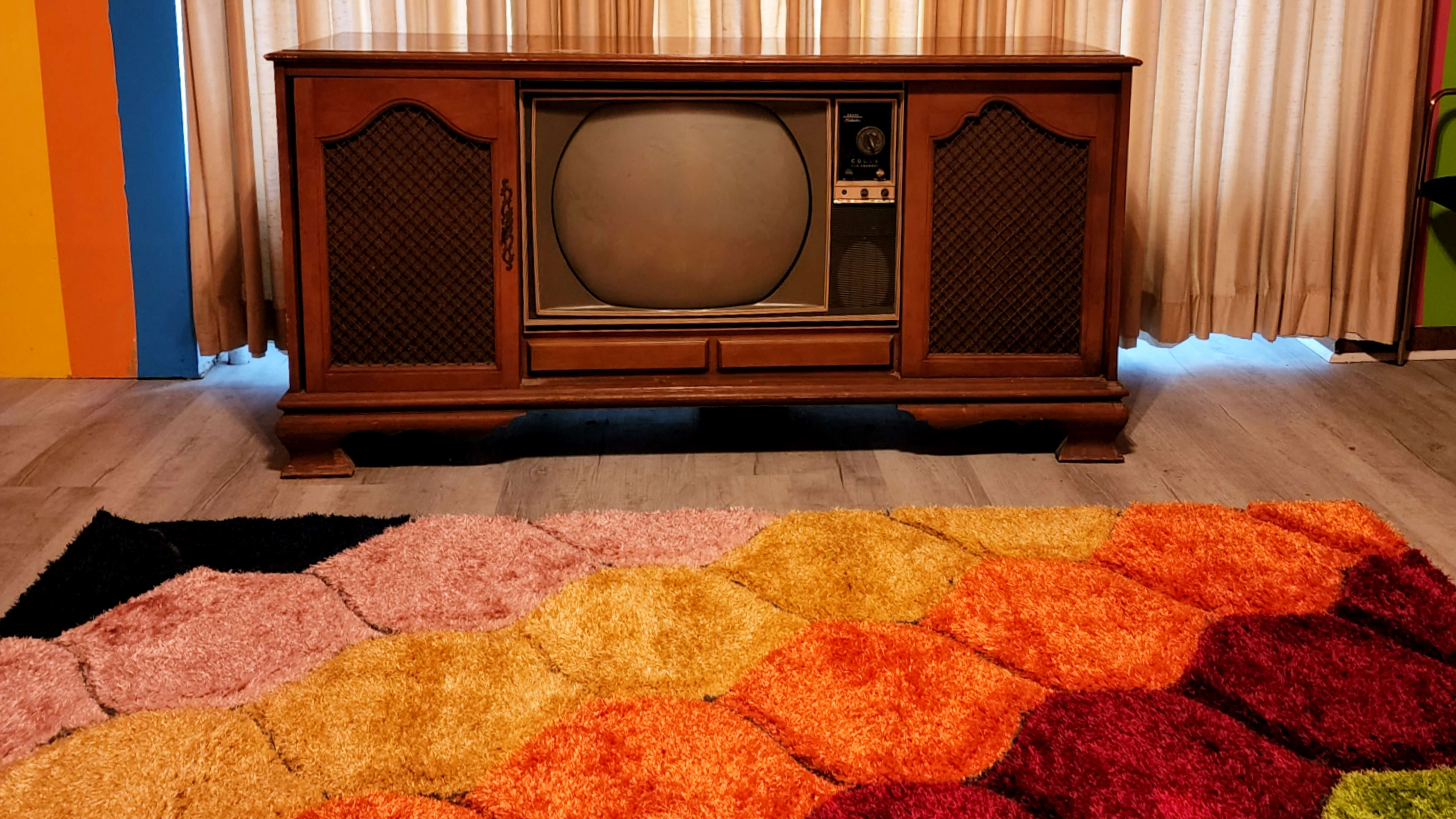 A vintage wooden television cabinet sits in front of a colorful, hexagon-patterned rug.