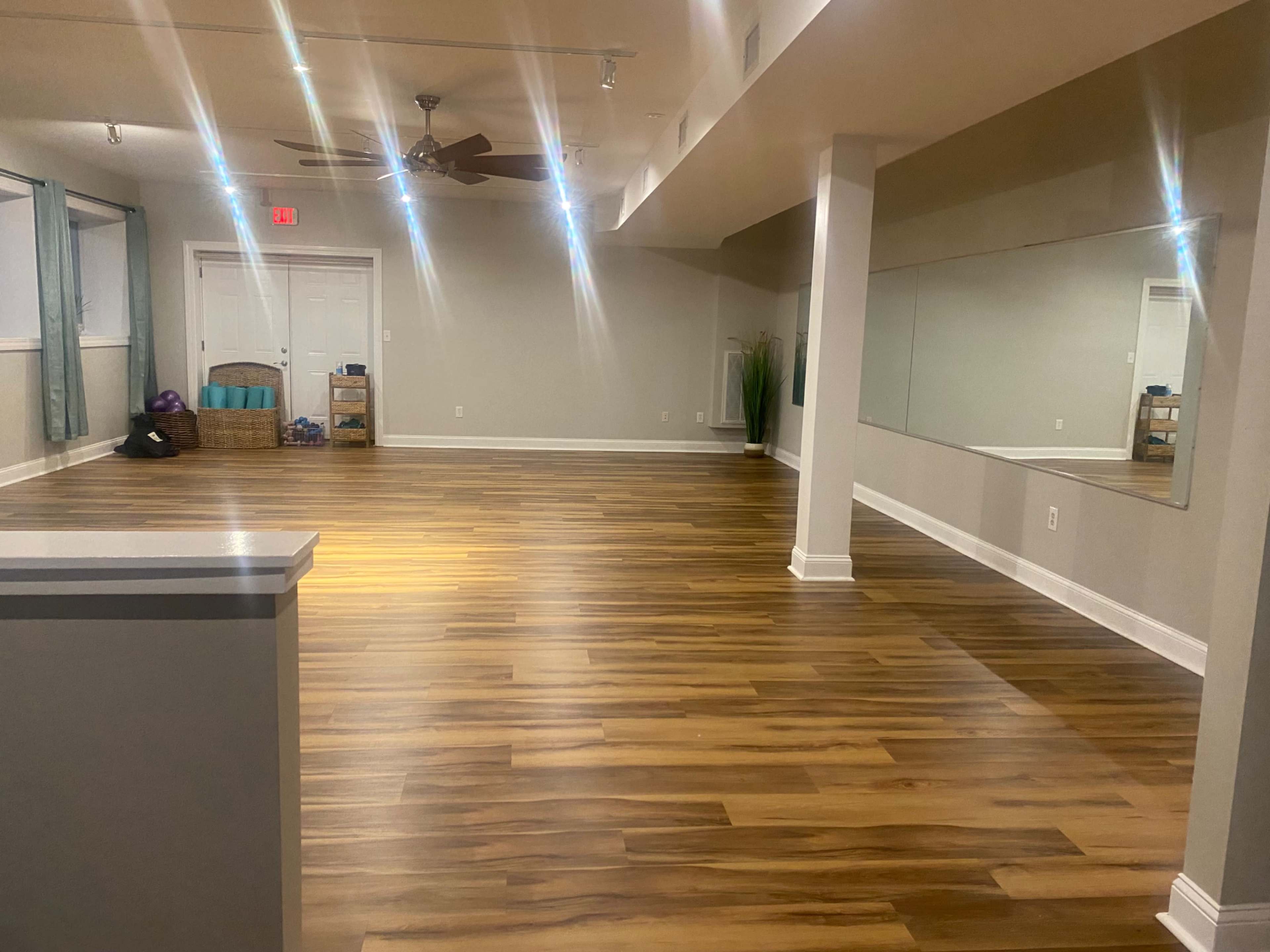 A spacious, empty room with wooden flooring, a ceiling fan, and a large mirror on one wall.