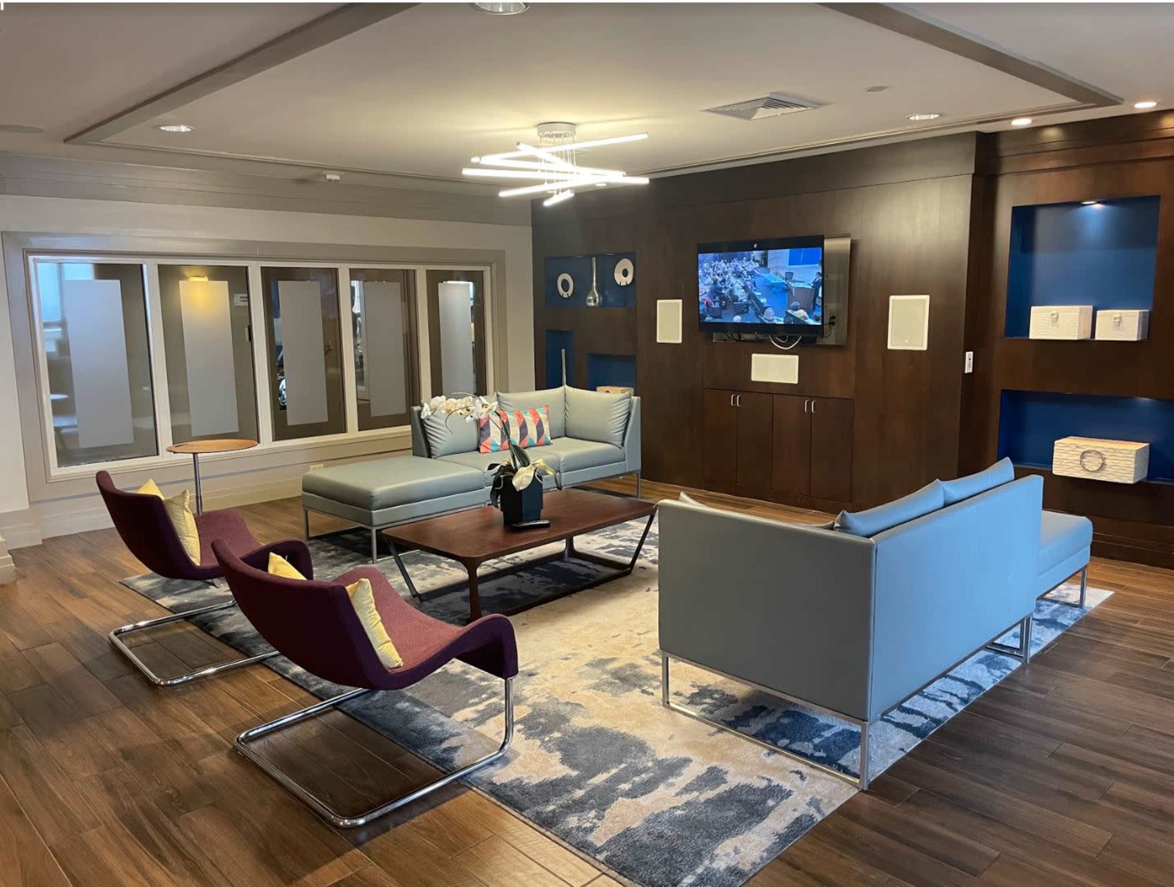 A modern lounge area with blue and purple seating, a large television mounted on a wooden wall, and decorative accents on shelves.