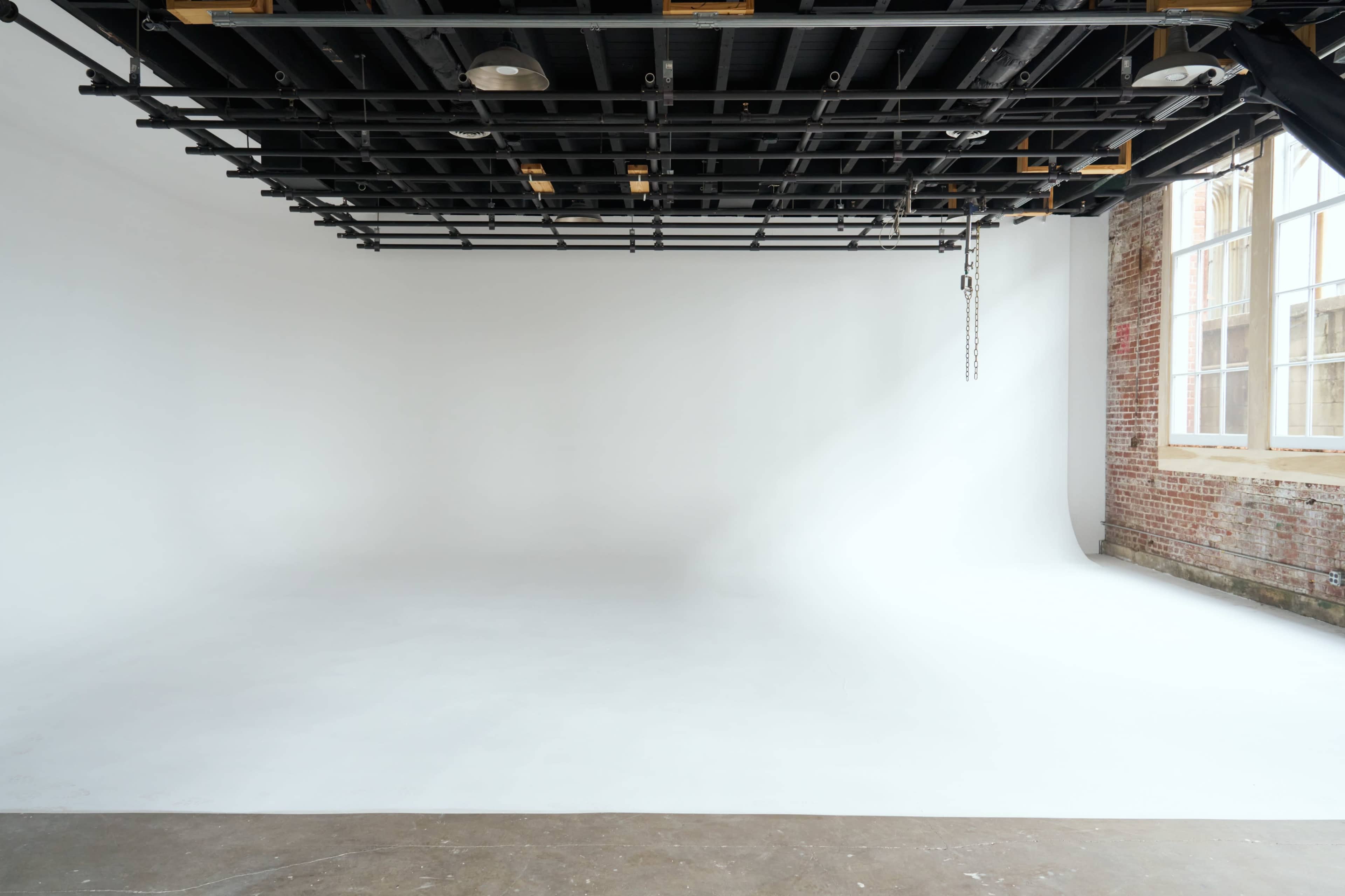 A spacious photography studio with a seamless white background and exposed brick walls.