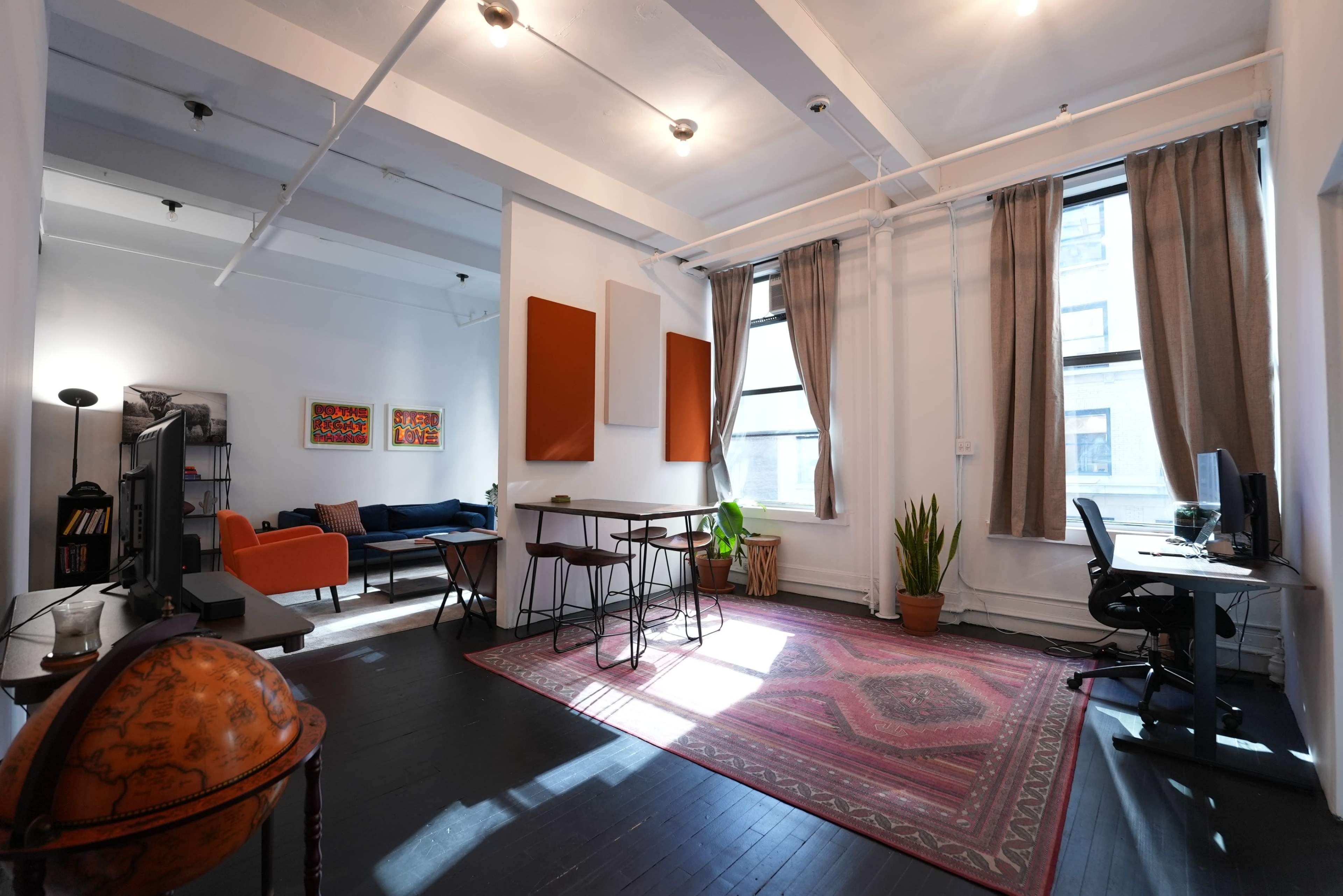 A well-lit, modern open-concept living space featuring a seating area, dining table, and a workspace with a computer.