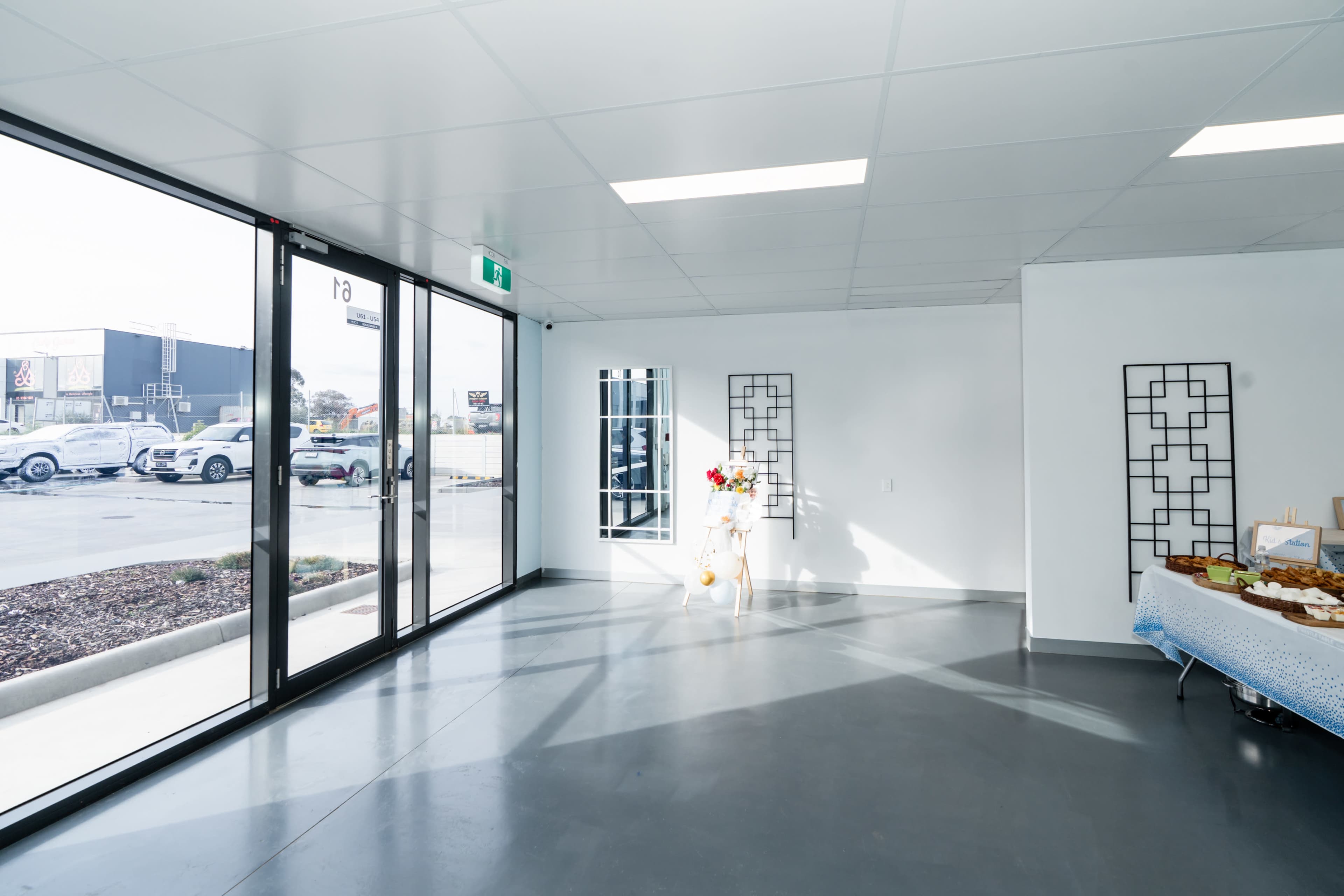 The image shows a spacious, empty interior with large glass doors, minimal furniture, and bright natural light entering from the outside.