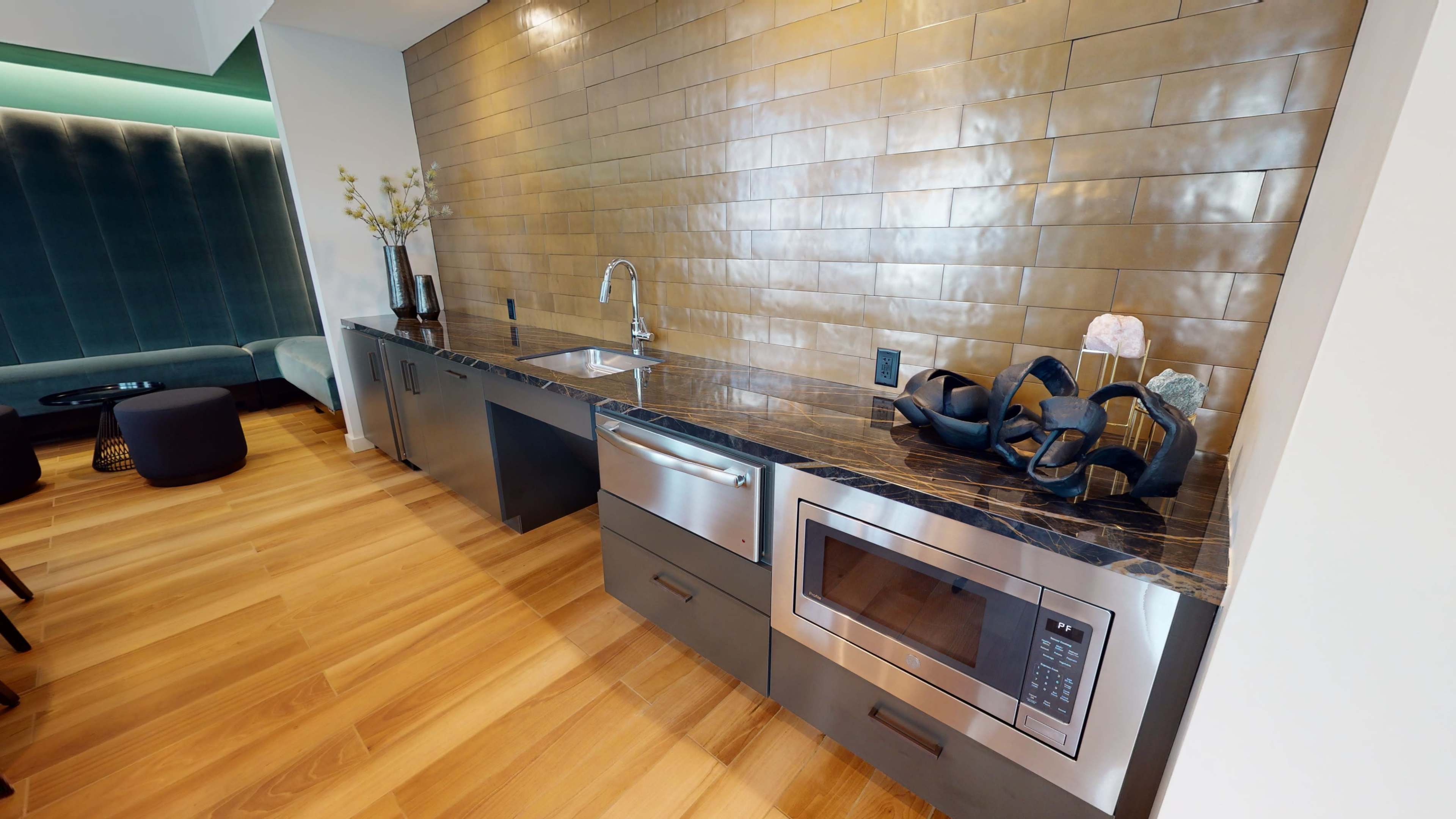 A modern kitchen with a polished stone countertop, a sink, a microwave, and decorative items on a backsplash made of square tiles.