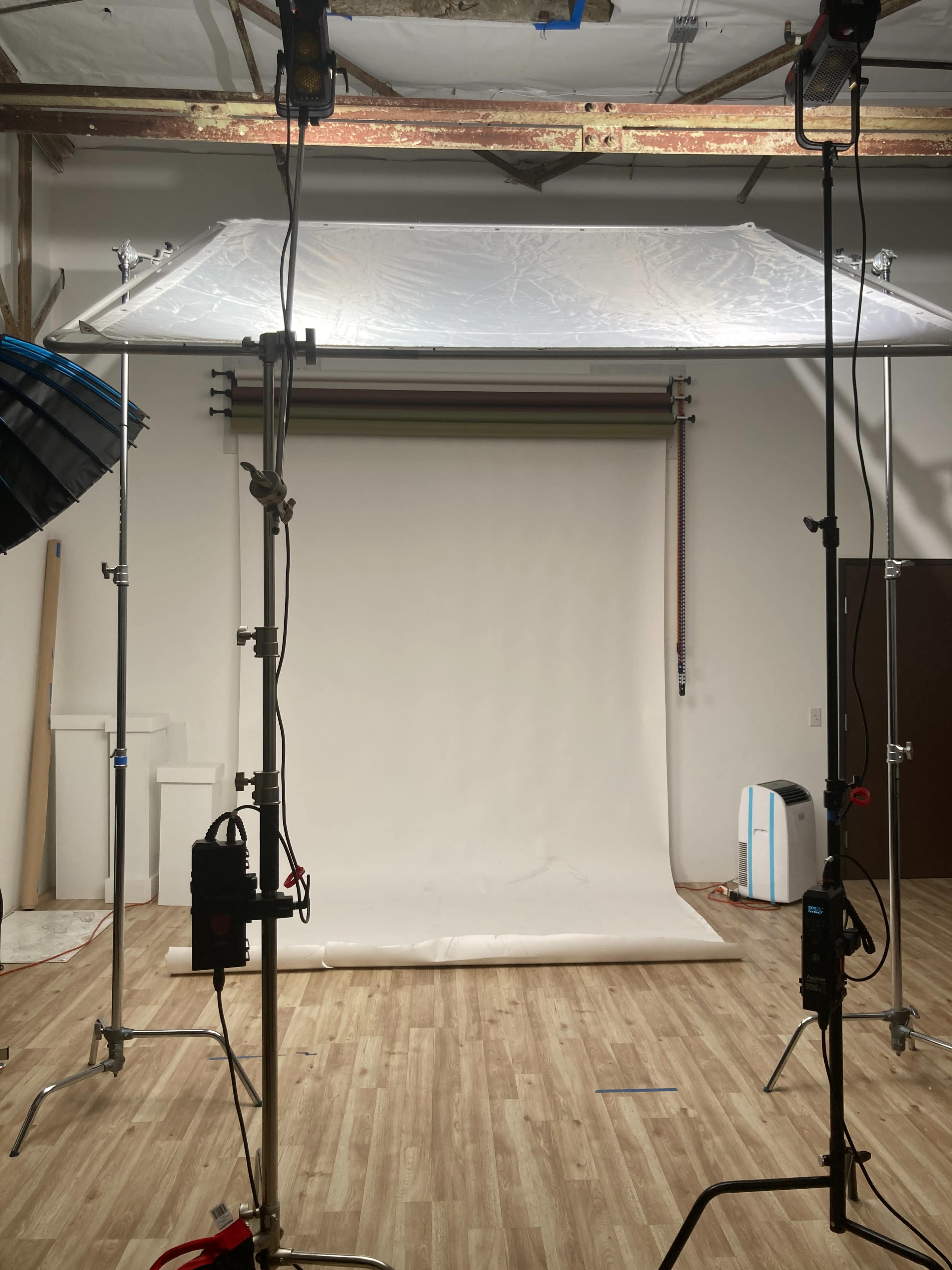 The image shows a photography studio setup with lighting equipment and a blank backdrop.