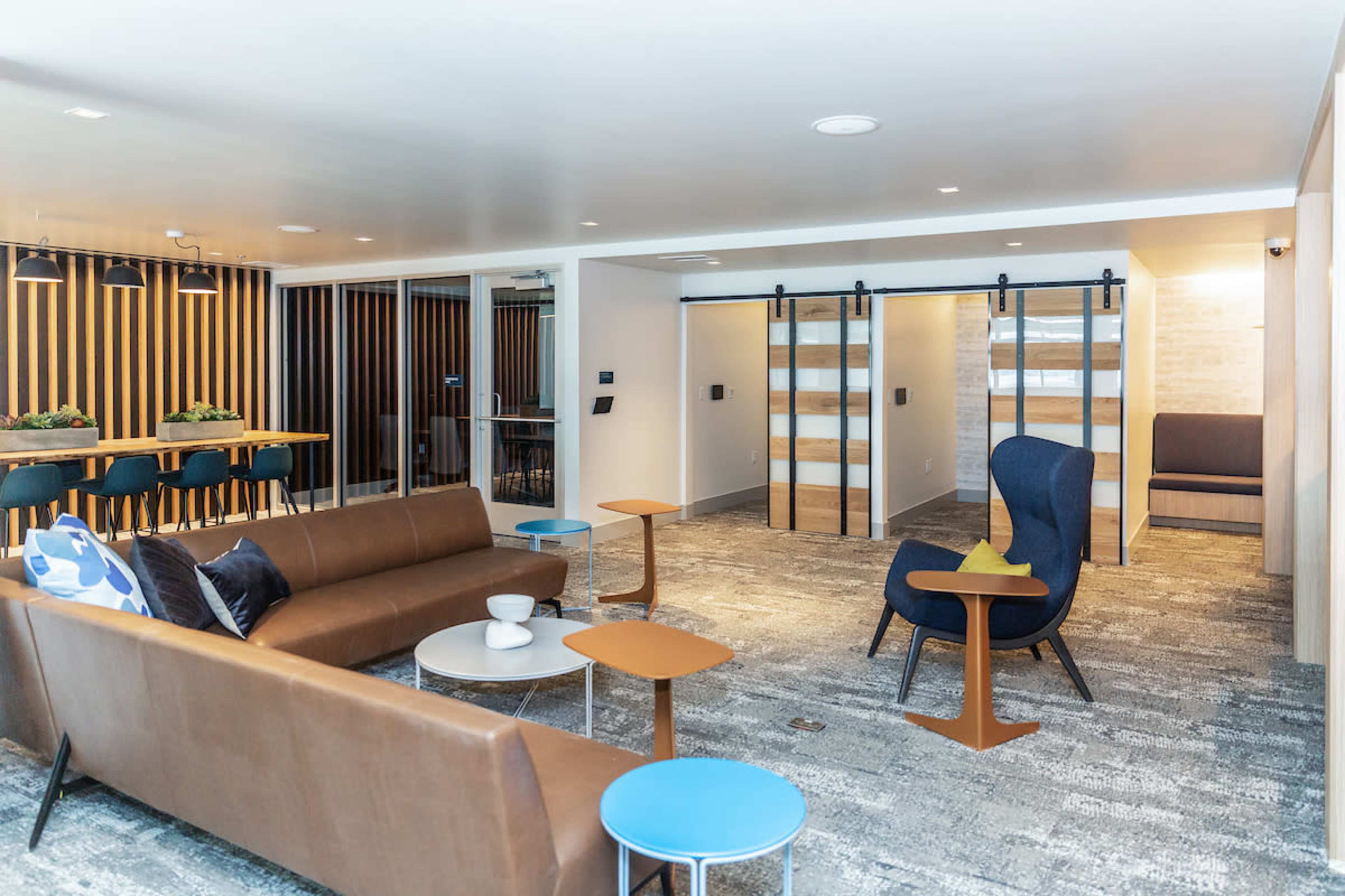 A modern lounge area featuring brown sofas, a blue chair, small tables, and wooden partition walls.