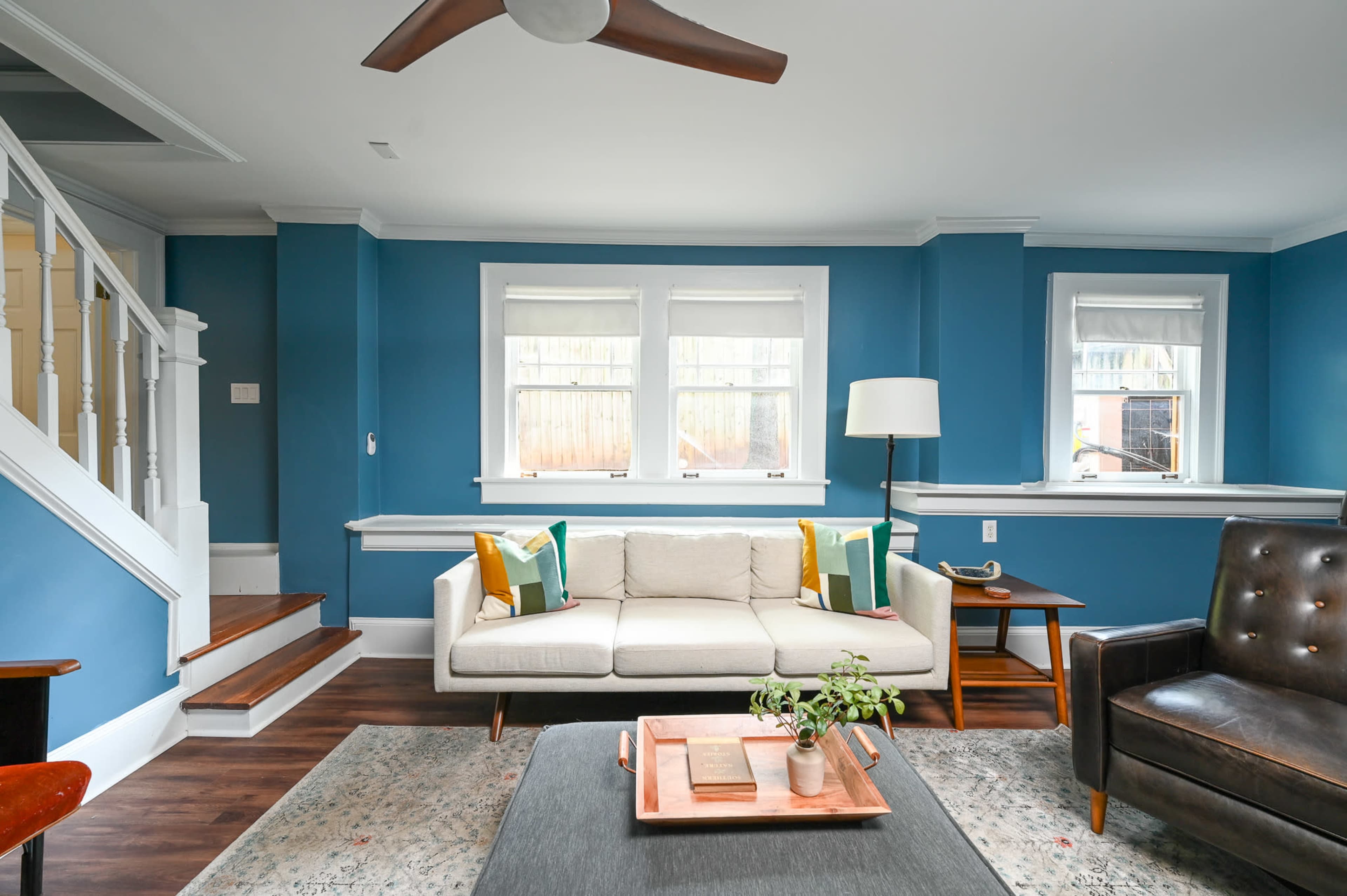A modern living room with a light-colored sofa, a dark armchair, a wooden table, and blue walls.