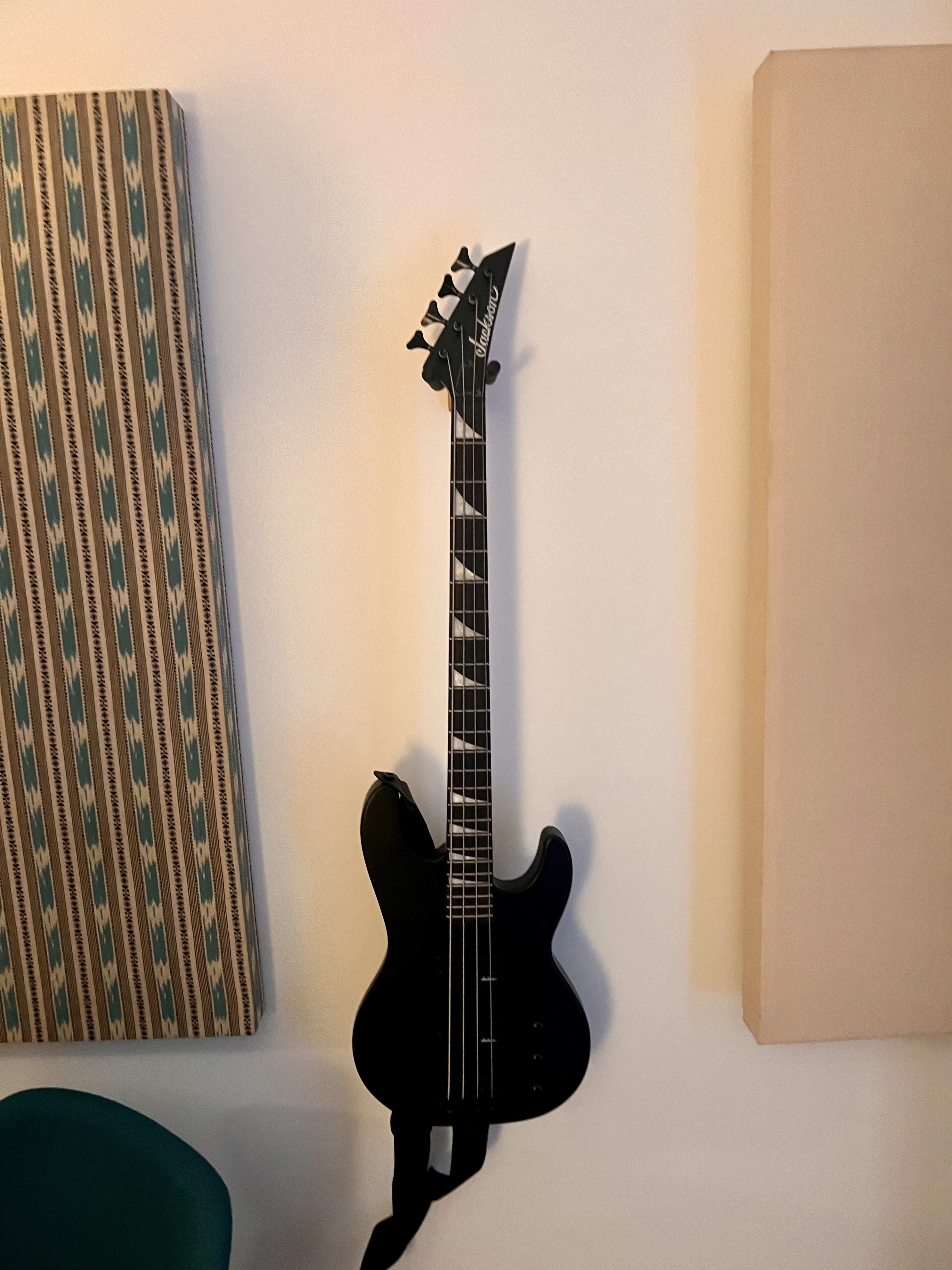 A black guitar is mounted on a white wall, flanked by two fabric-covered panels.