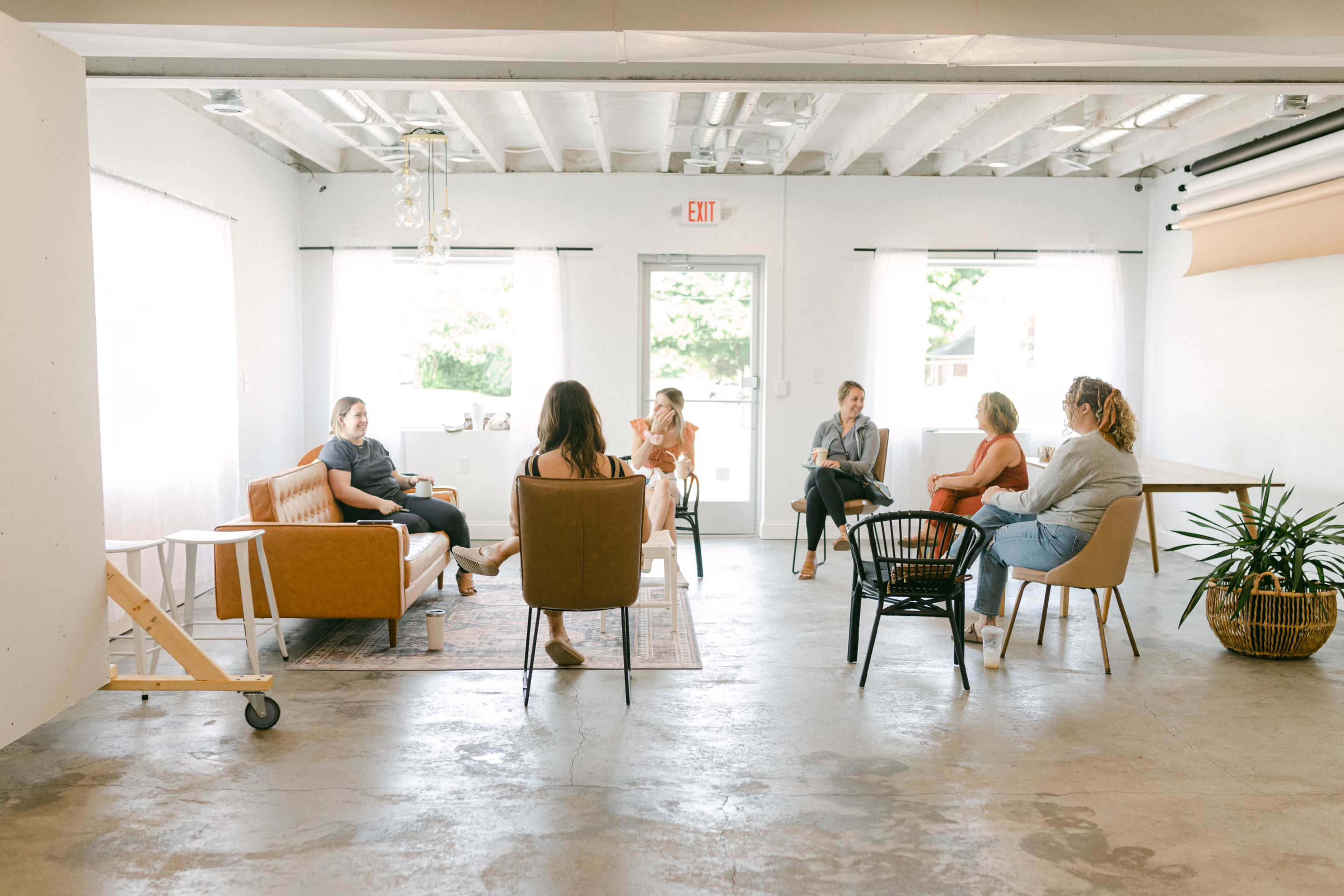 A group of six people sits in a well-lit room with modern furnishings, engaging in a discussion.