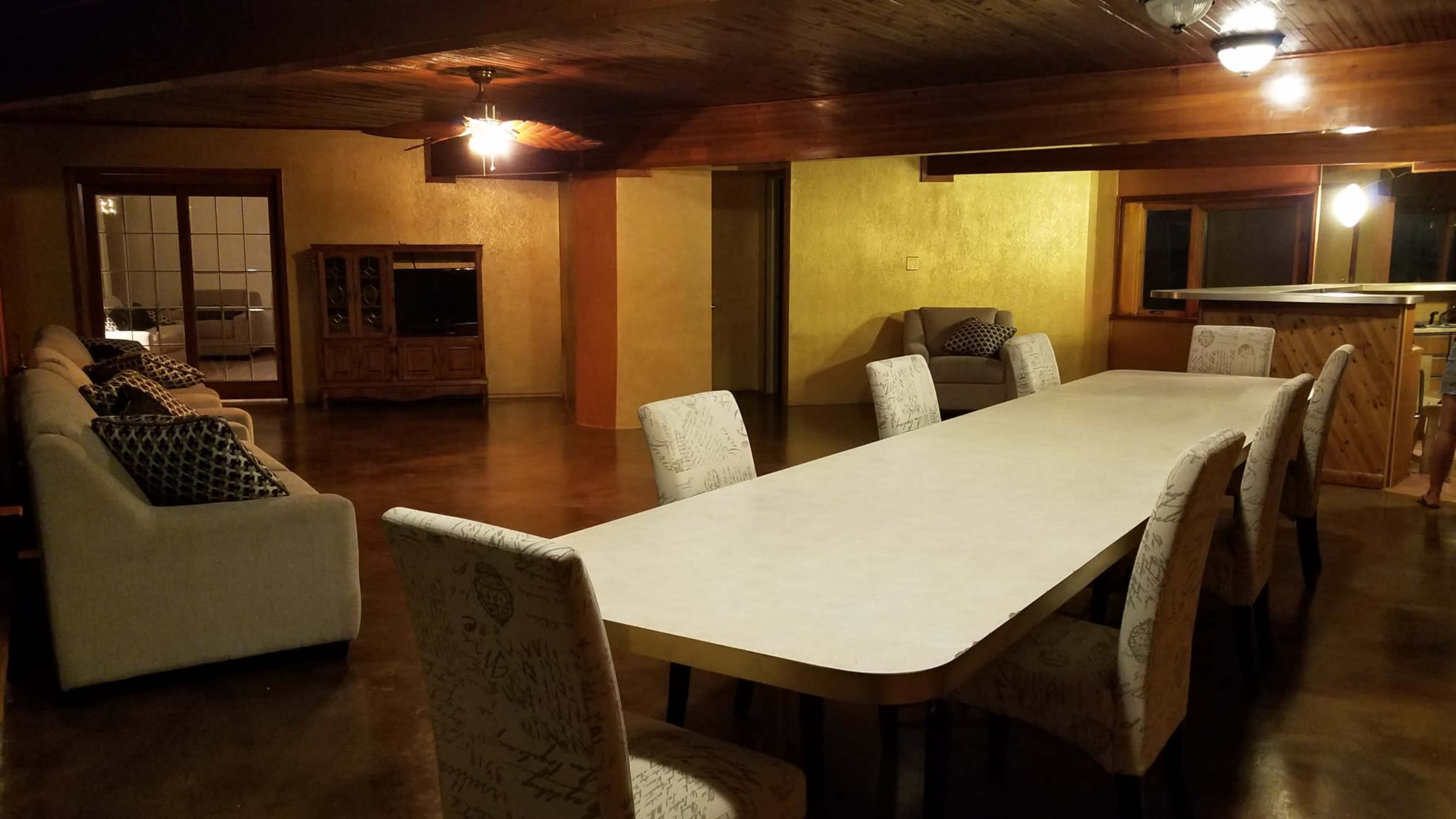A spacious room features a long dining table surrounded by chairs, with sofas arranged along one side.