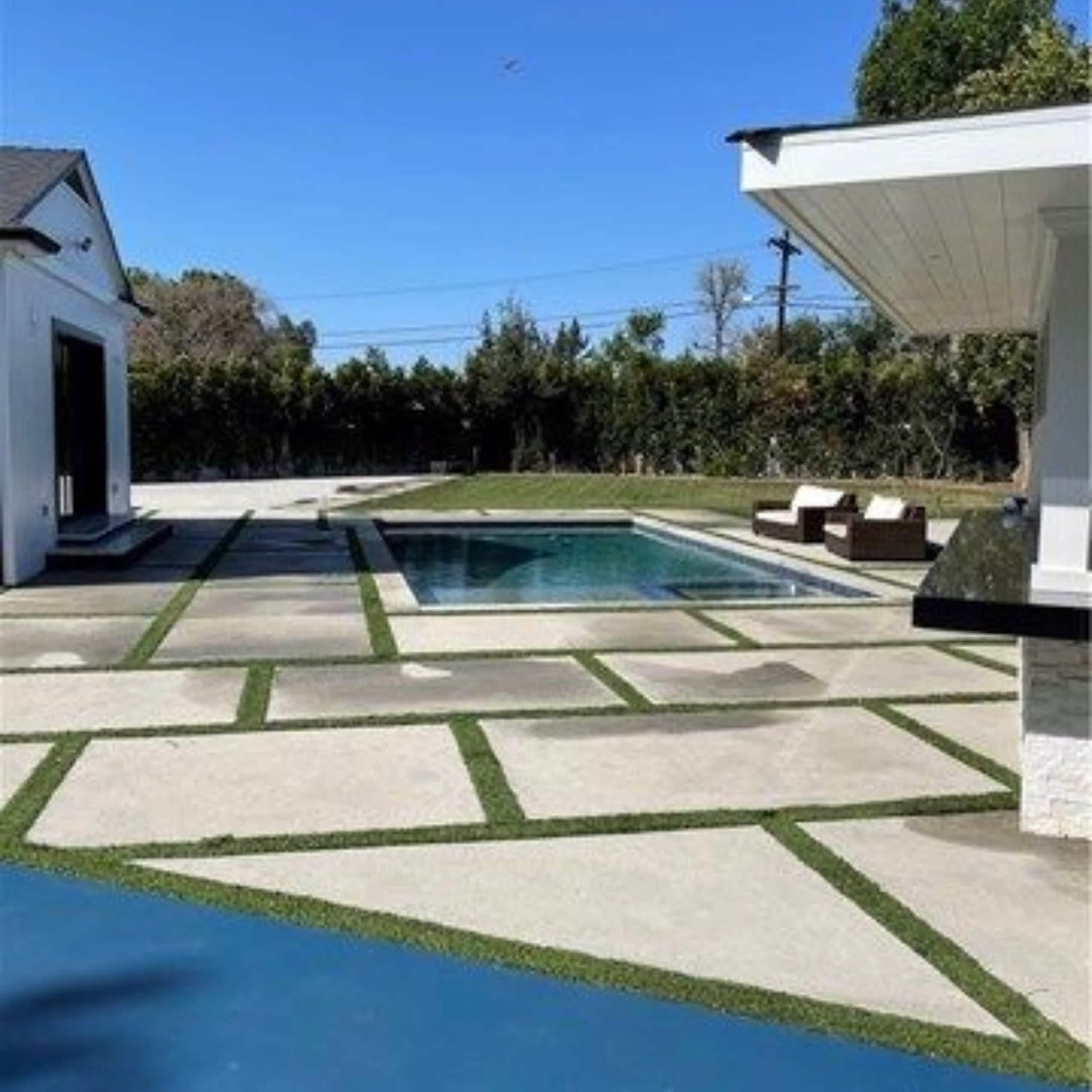 A modern backyard featuring a swimming pool surrounded by concrete slabs and green grass accents.