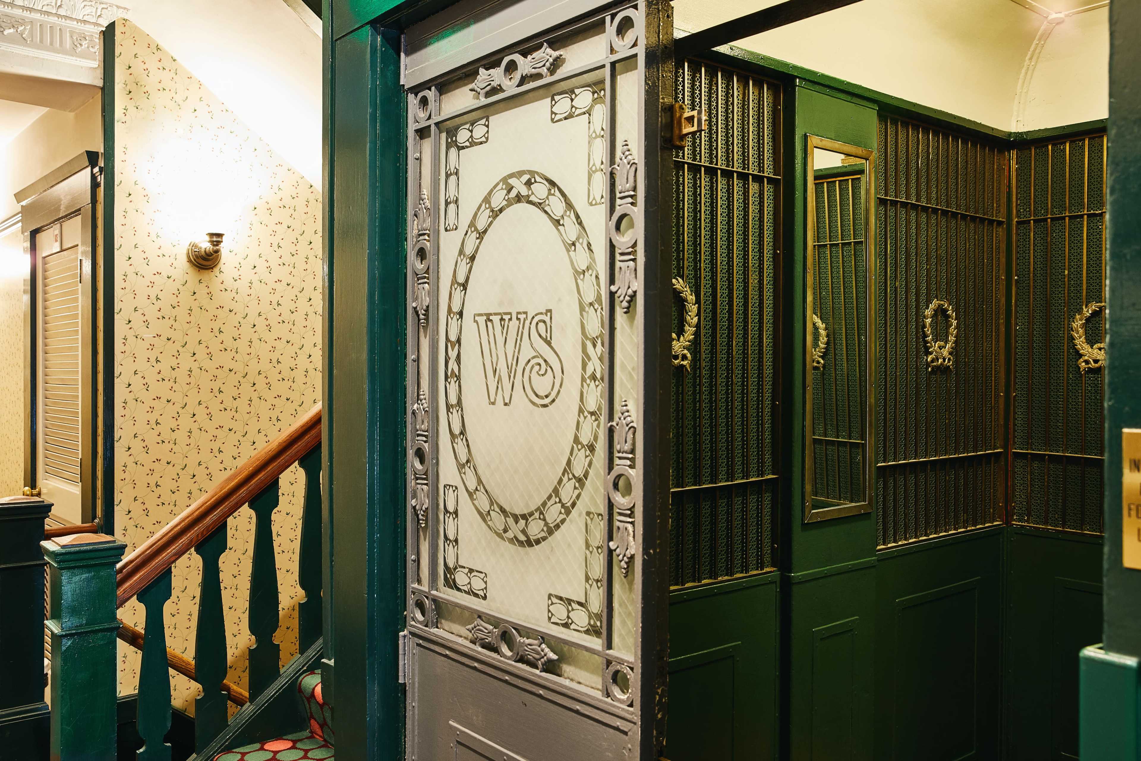 A vintage elevator entrance with ornate details and a patterned wallpapered hallway.