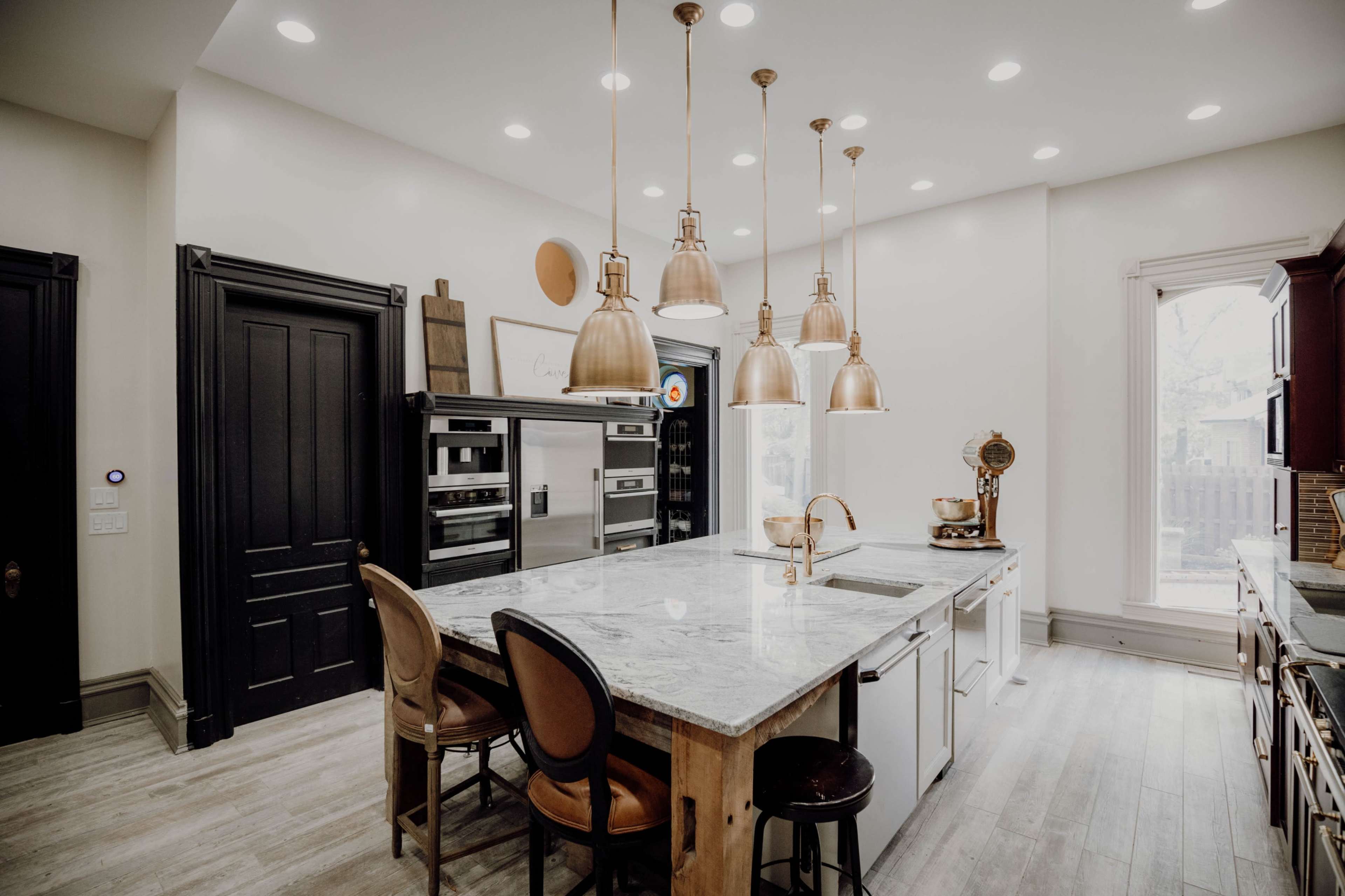 A modern kitchen features a large island with seating, pendant lights above, and stainless steel appliances.