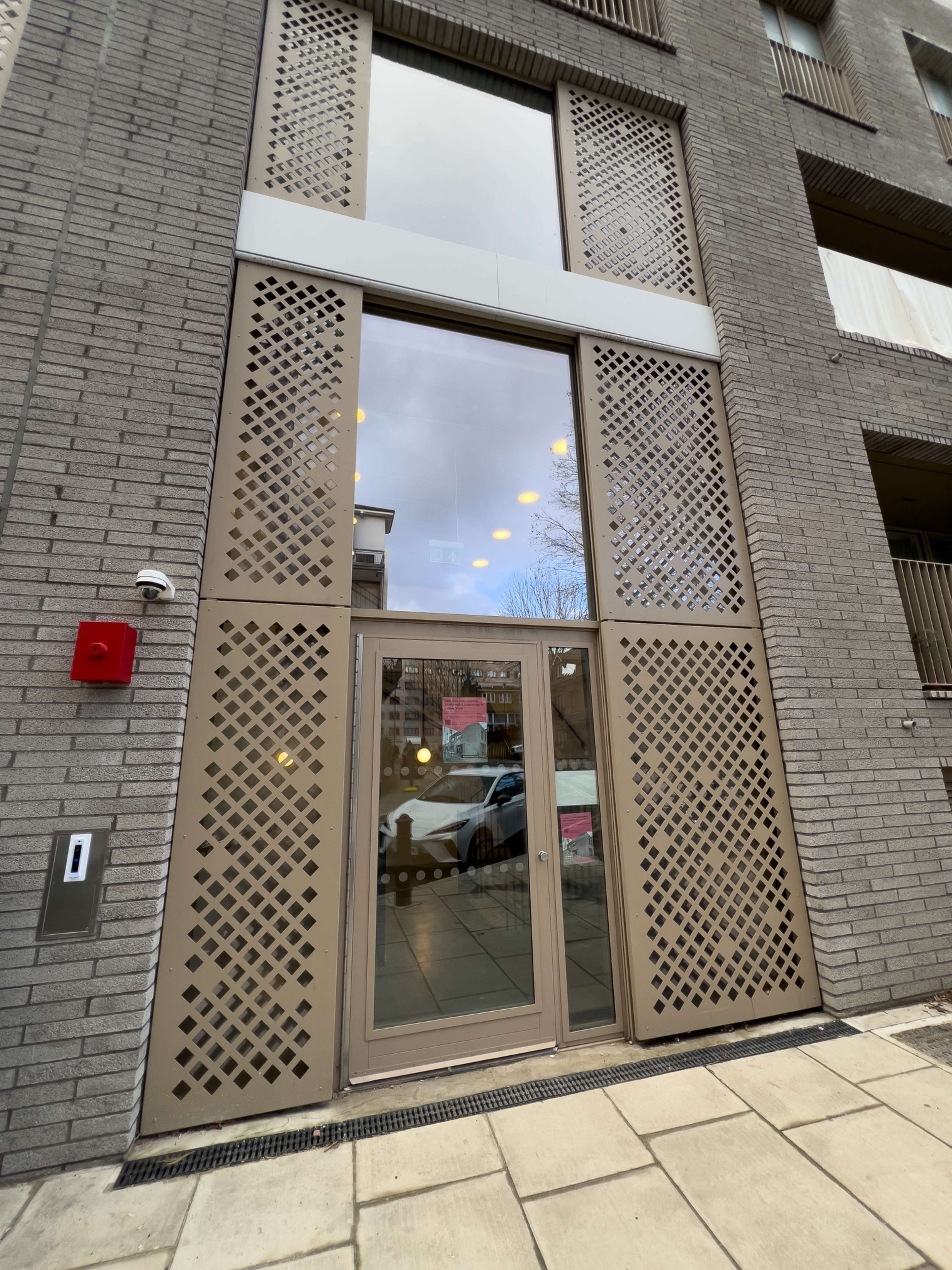 The image shows a modern building facade with a large, decorative entrance door and a grid-patterned design above it.