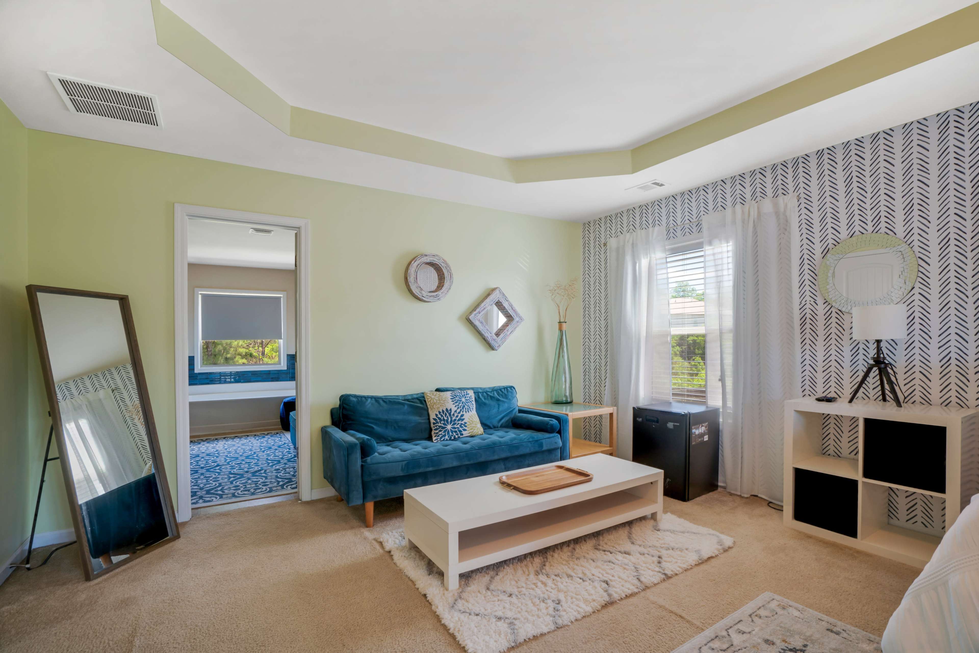The image shows a well-decorated living room with a green accent wall, a blue sofa, a coffee table, and a mirror reflecting the space.