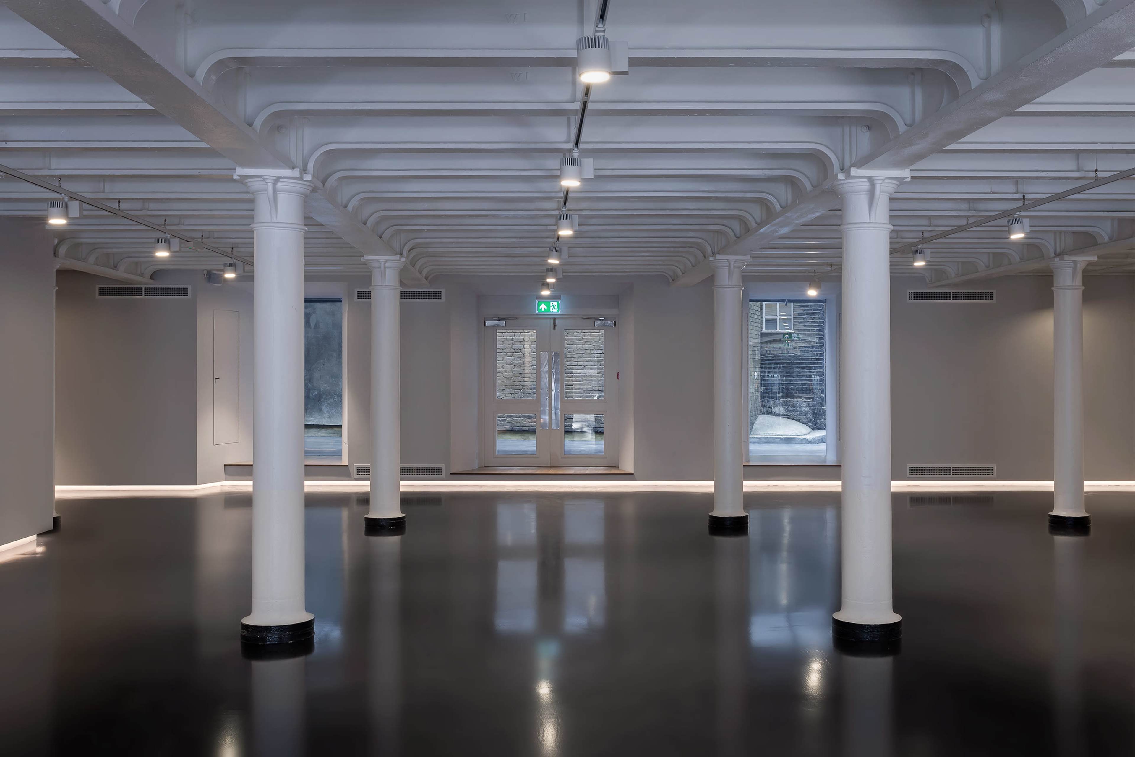 A spacious, modern interior with white columns, polished dark flooring, and exposed ceiling beams.