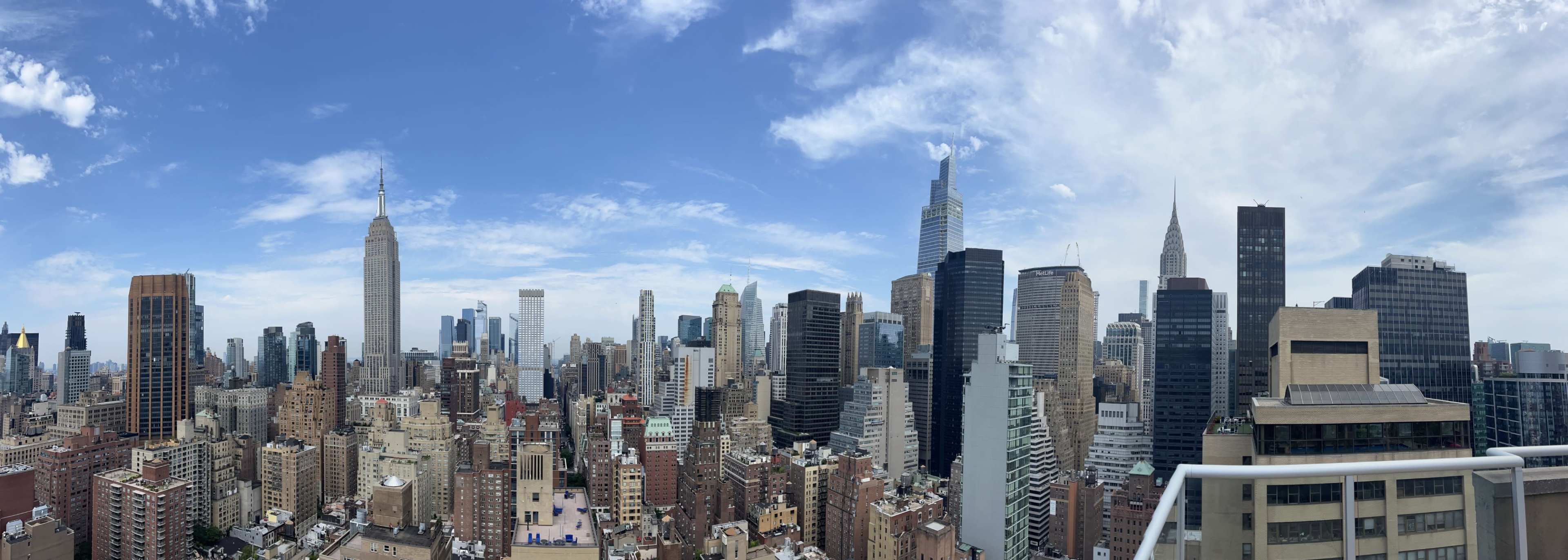 A panoramic view of the New York City skyline featuring various skyscrapers under a partly cloudy sky.