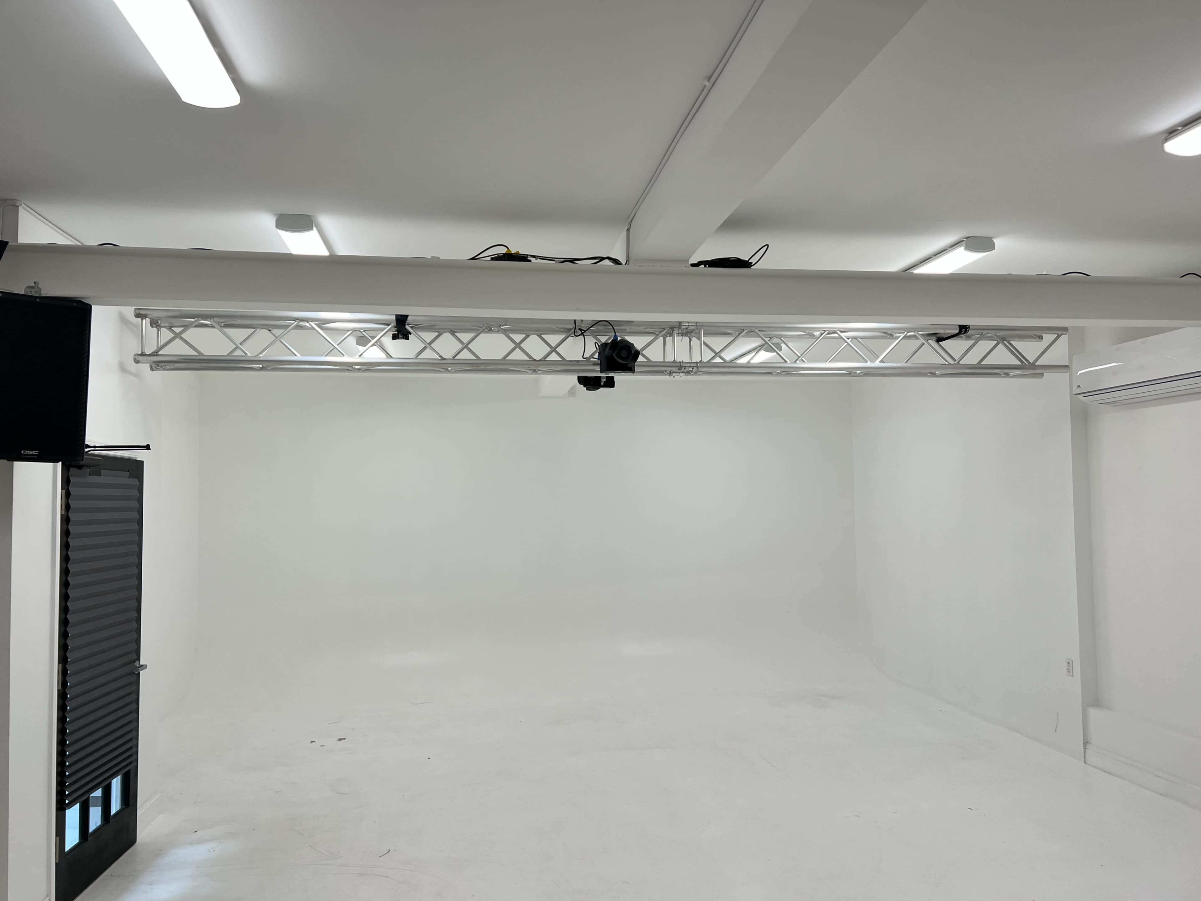 An empty studio space with a white background and lighting fixtures mounted on a truss above.