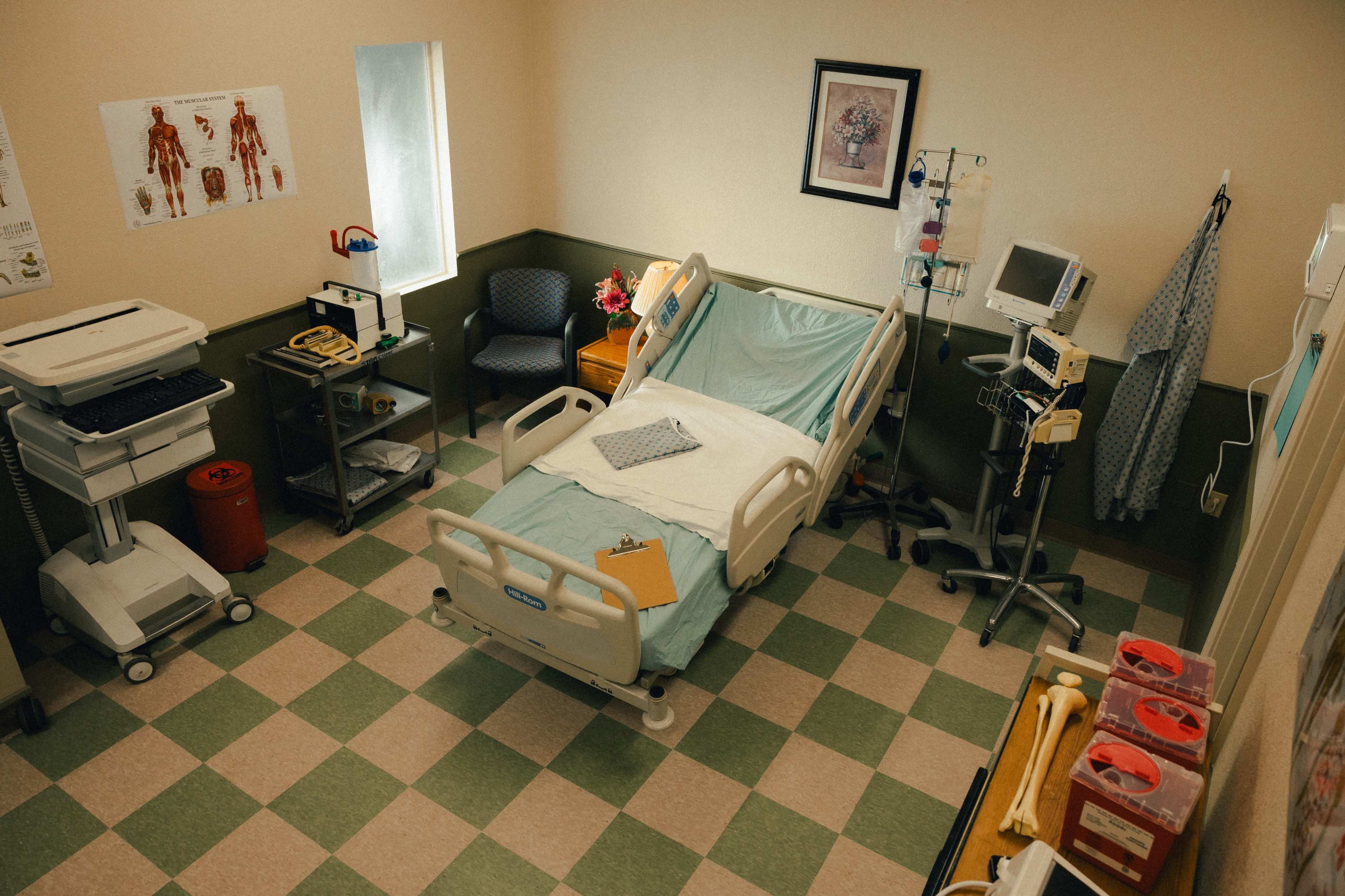 A hospital room featuring a patient bed, medical equipment, and charts on the walls.