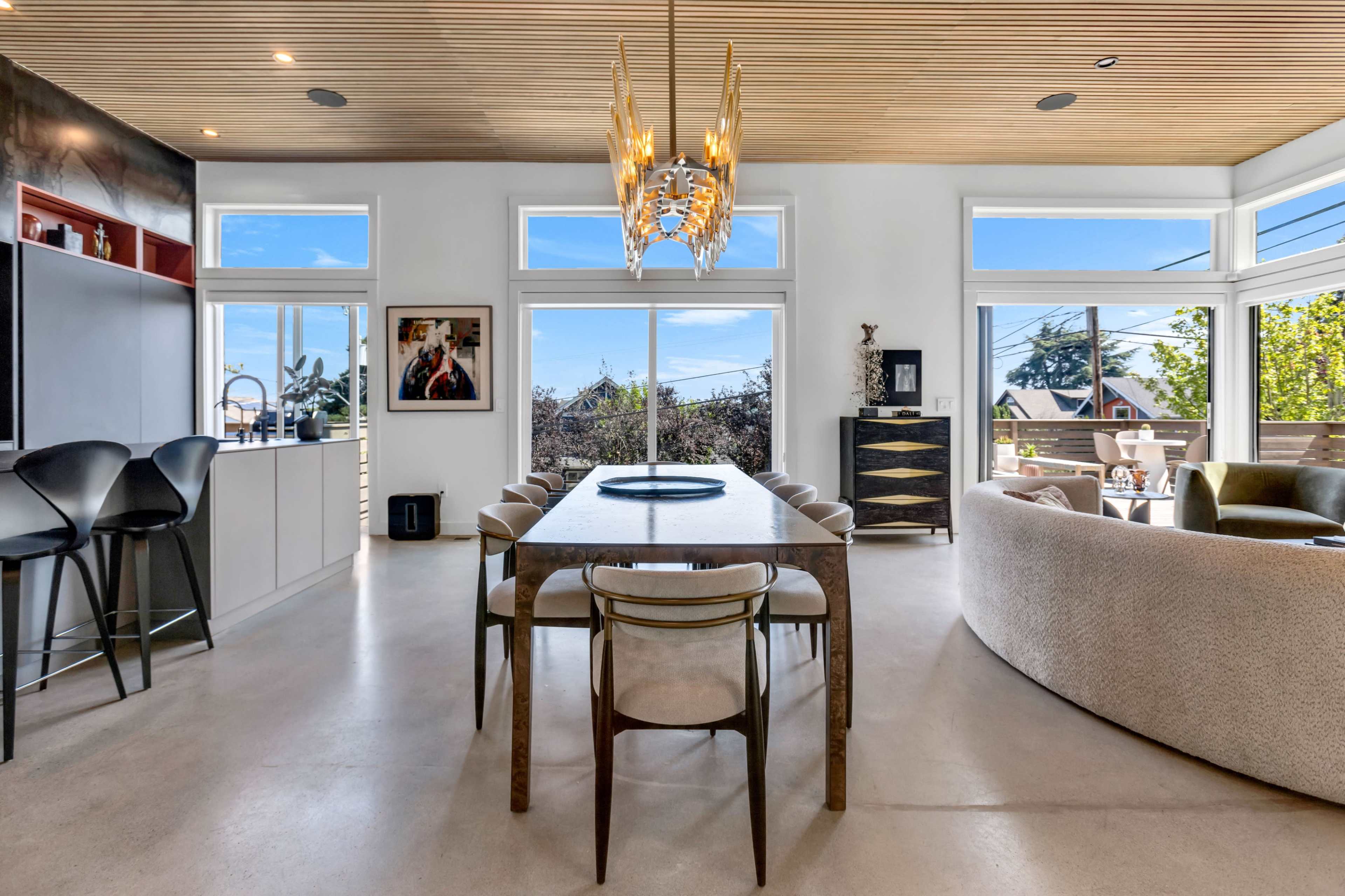 The image shows a modern dining area with a long table, stylish chairs, and large windows allowing natural light to fill the space.