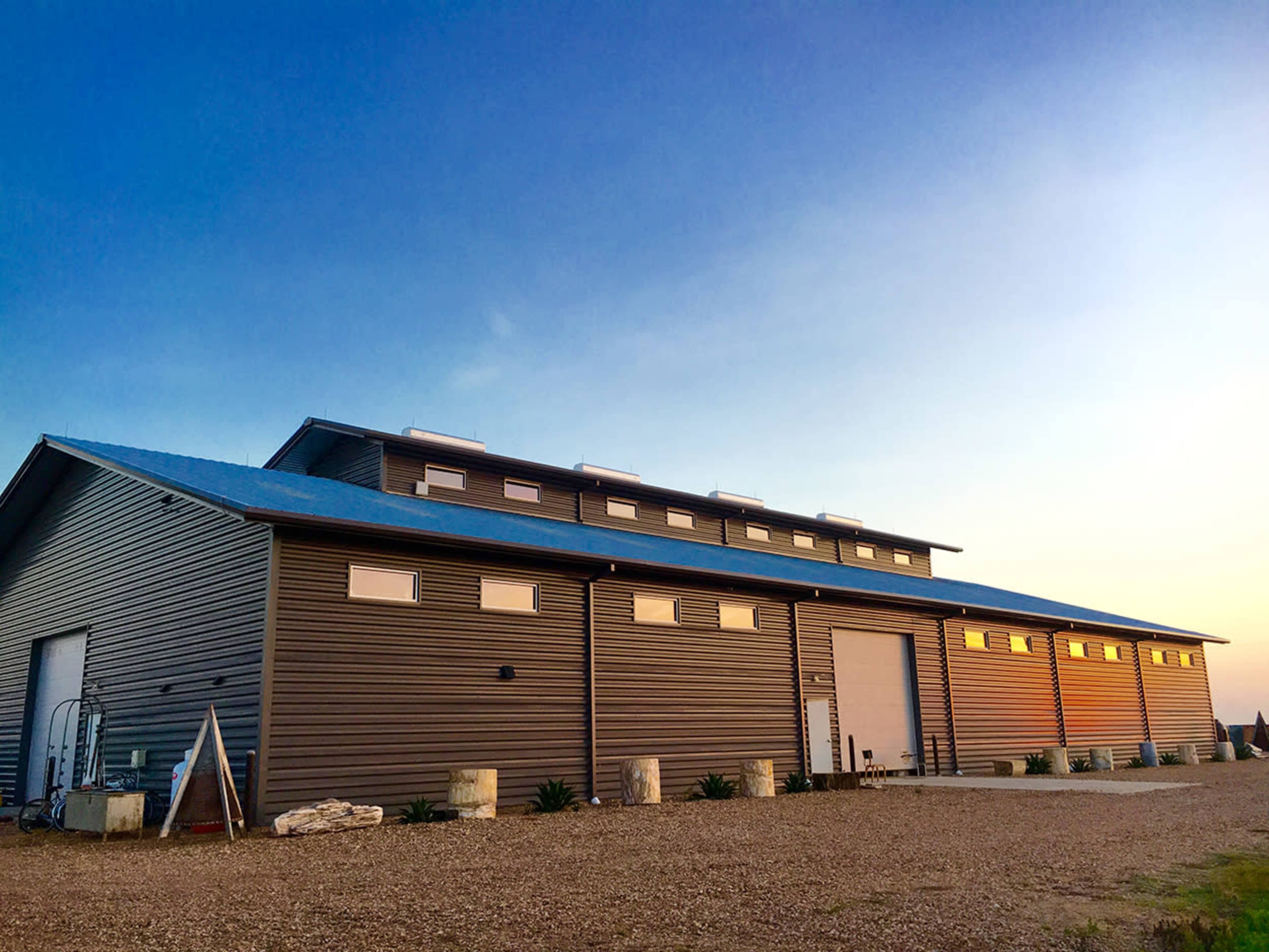 A large metal building with a blue roof and several garage doors stands against a clear sky at sunset.