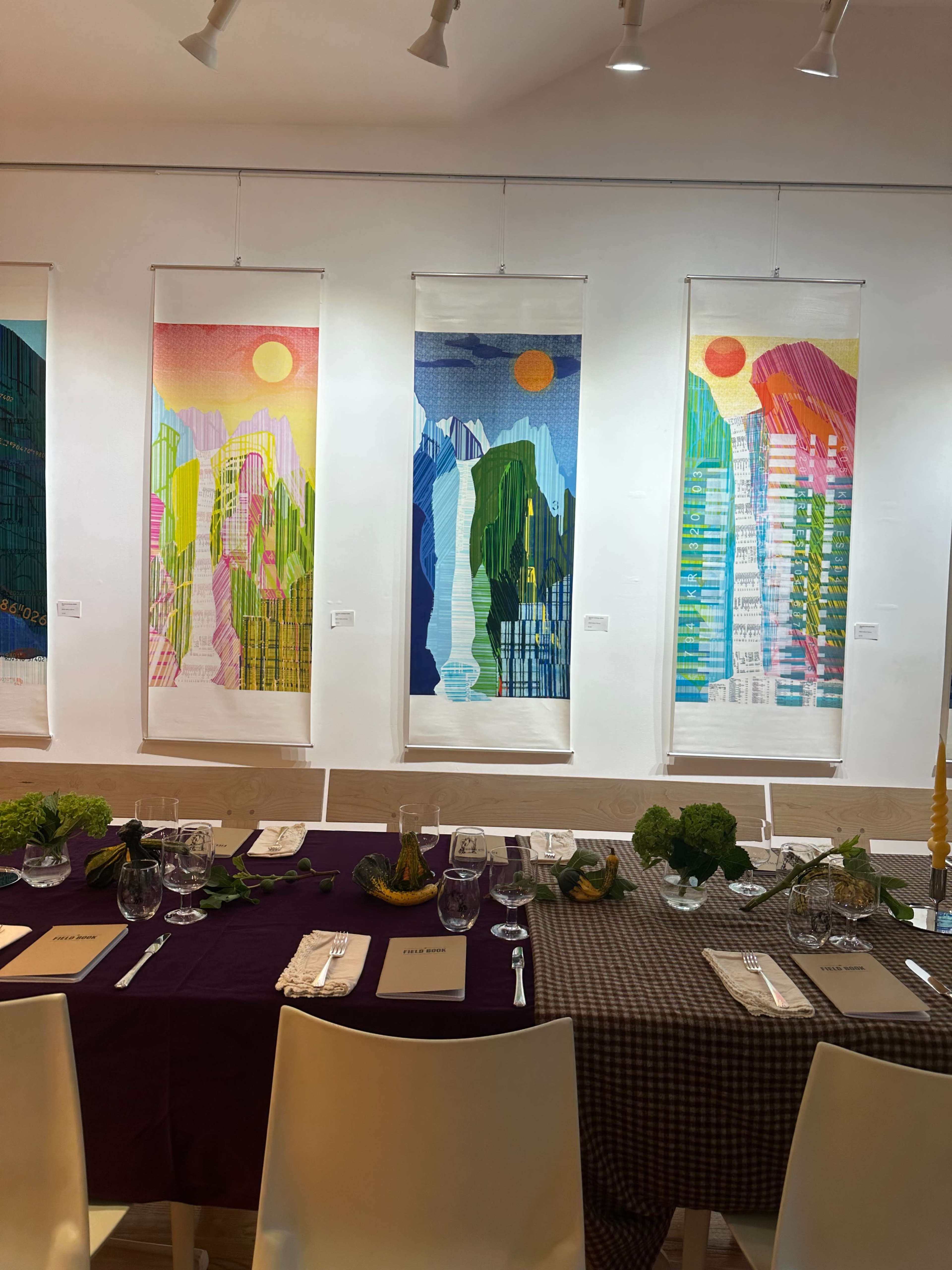 A dining table is set in front of colorful mountain-themed artwork displayed on the wall.