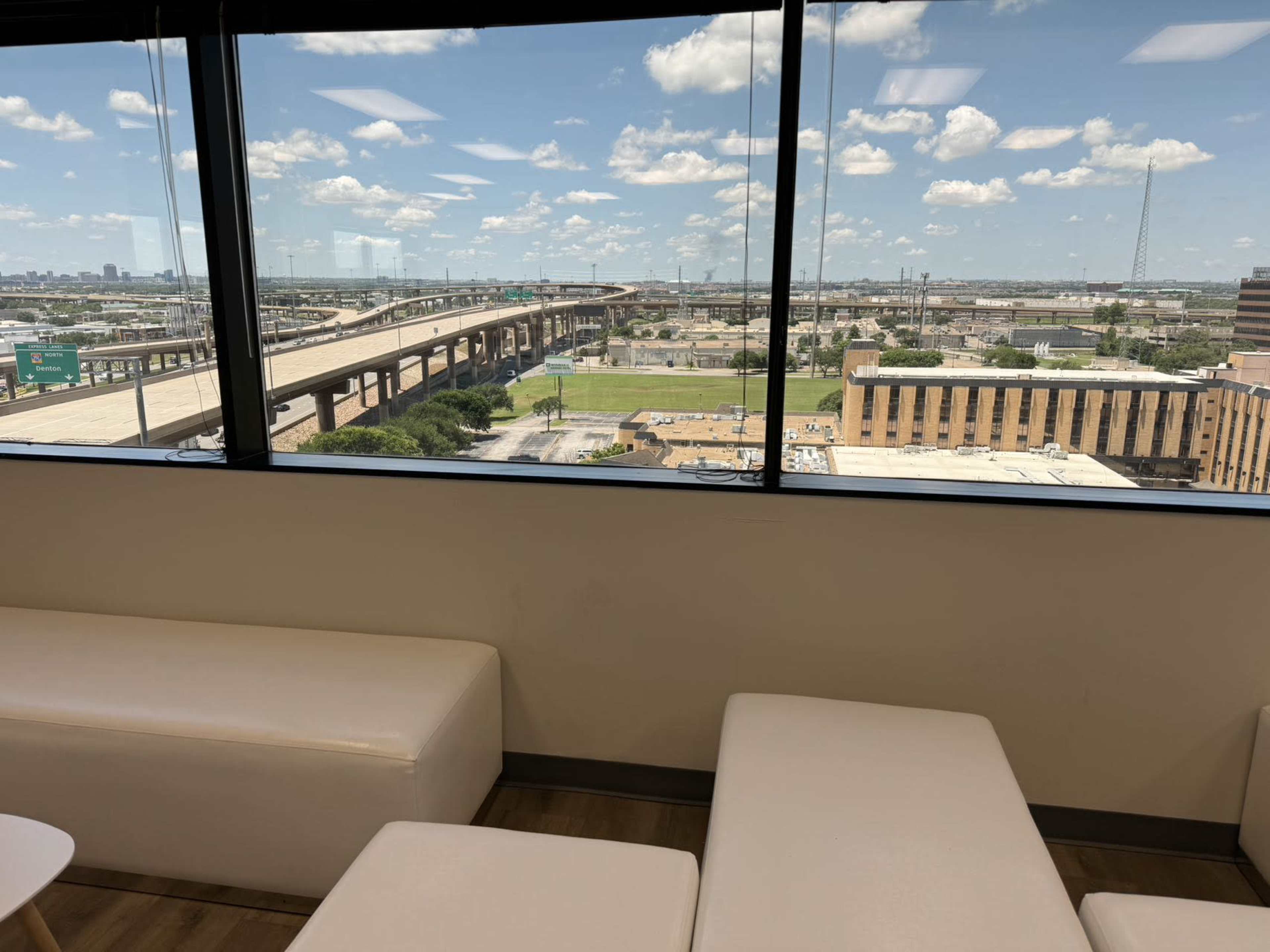 A view of a city landscape with highways and buildings visible through a large window, along with a white seating area in the foreground.