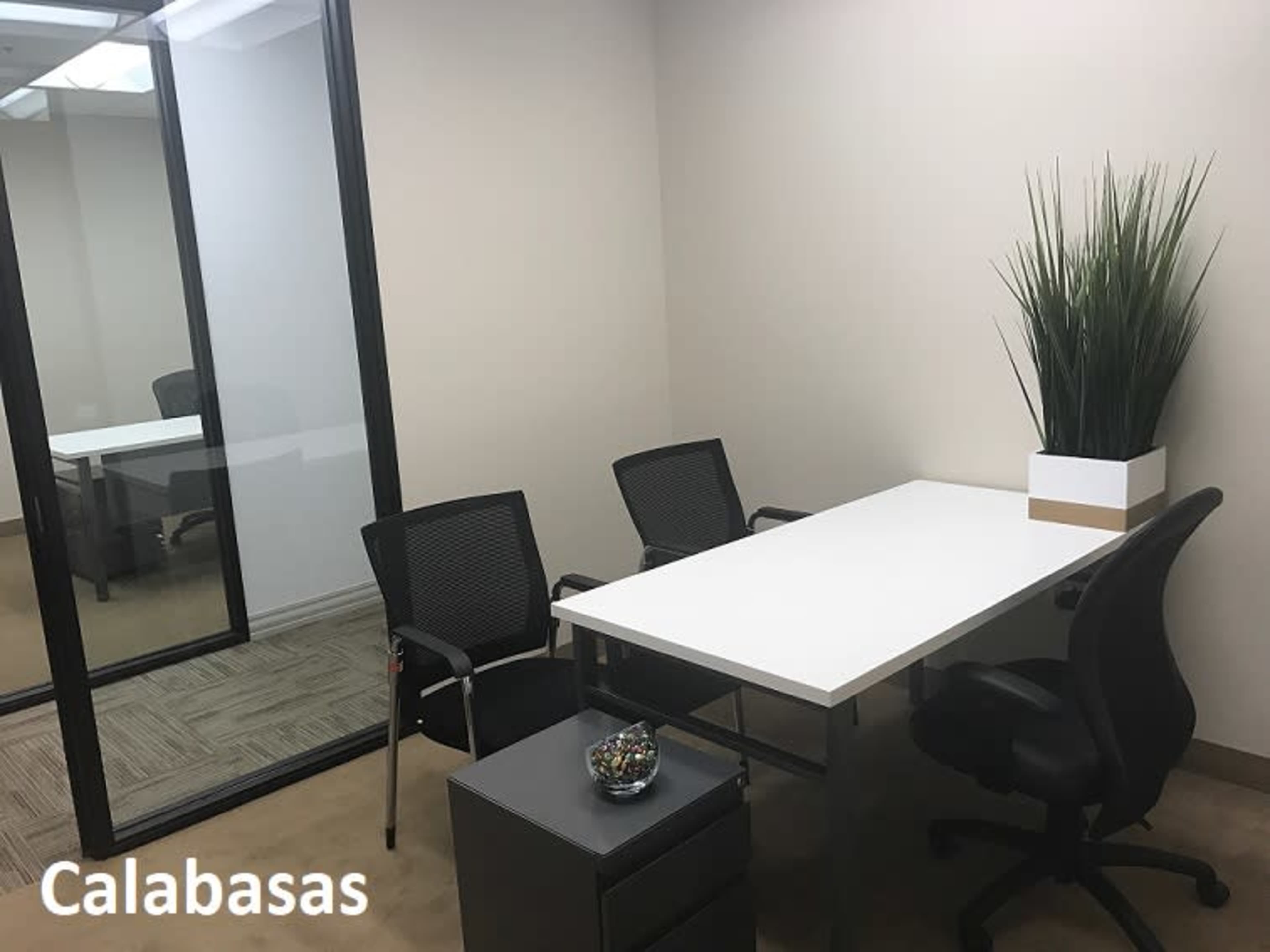 A small office space featuring a white table, two black chairs, a filing cabinet, and a potted plant.