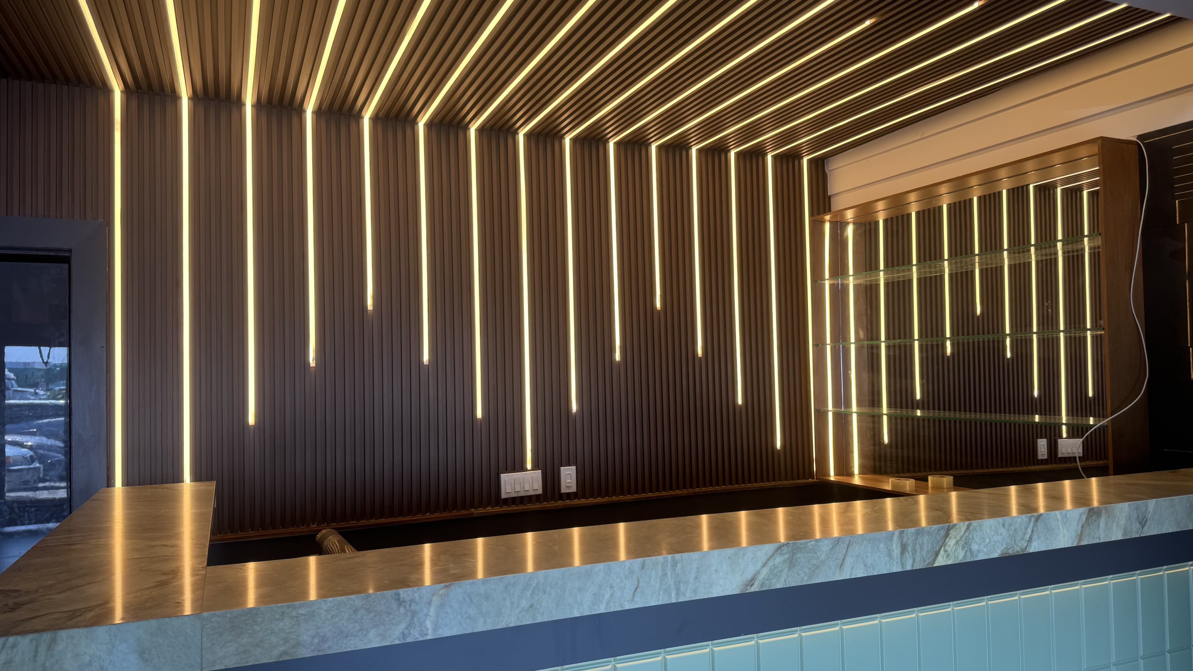 The image shows a modern reception area featuring a sleek counter with a marble surface, illuminated by vertical LED strip lights along the wall and ceiling.