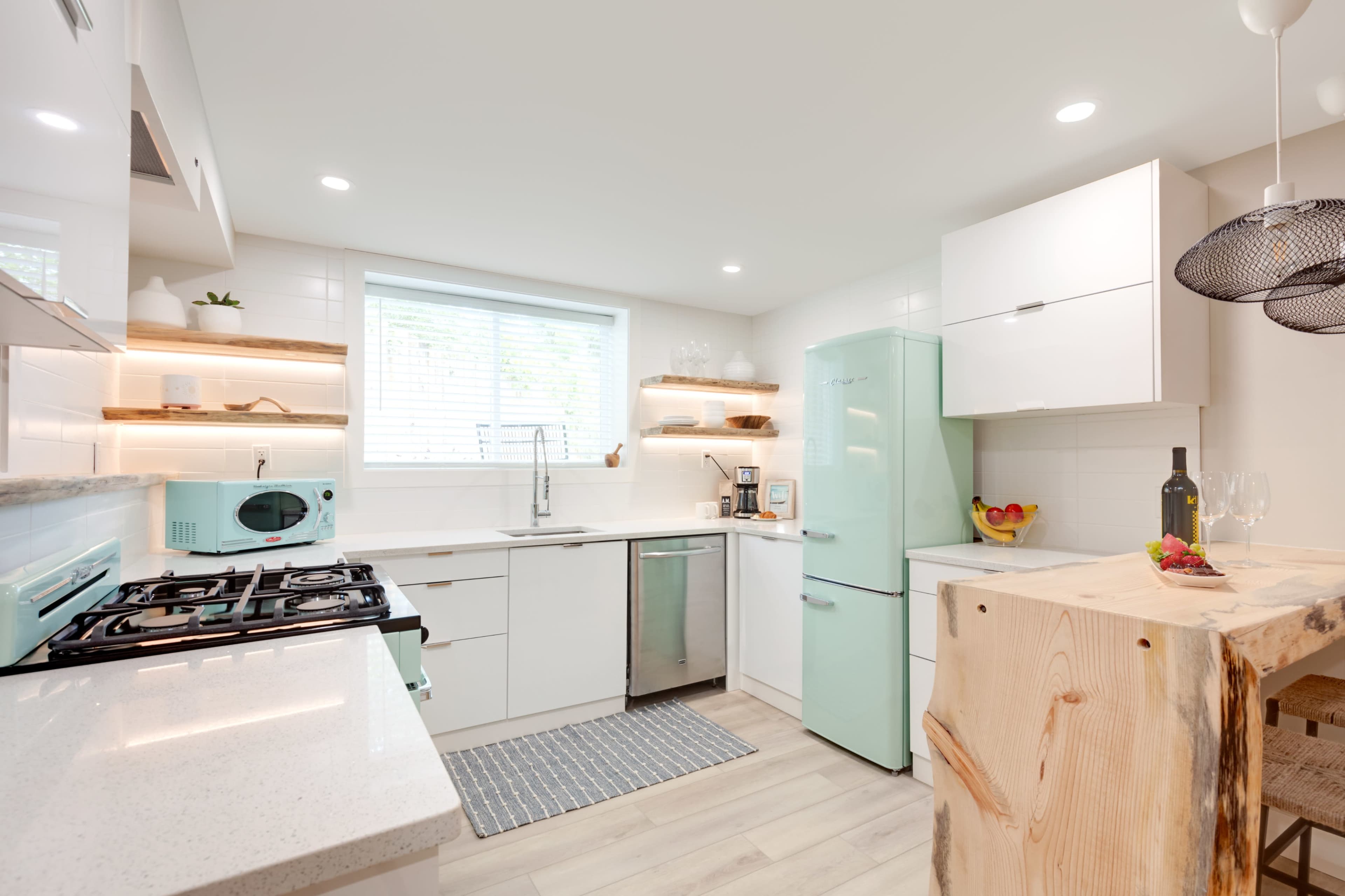 The kitchen features white cabinetry, a mint green refrigerator, and wooden open shelves above a countertop.