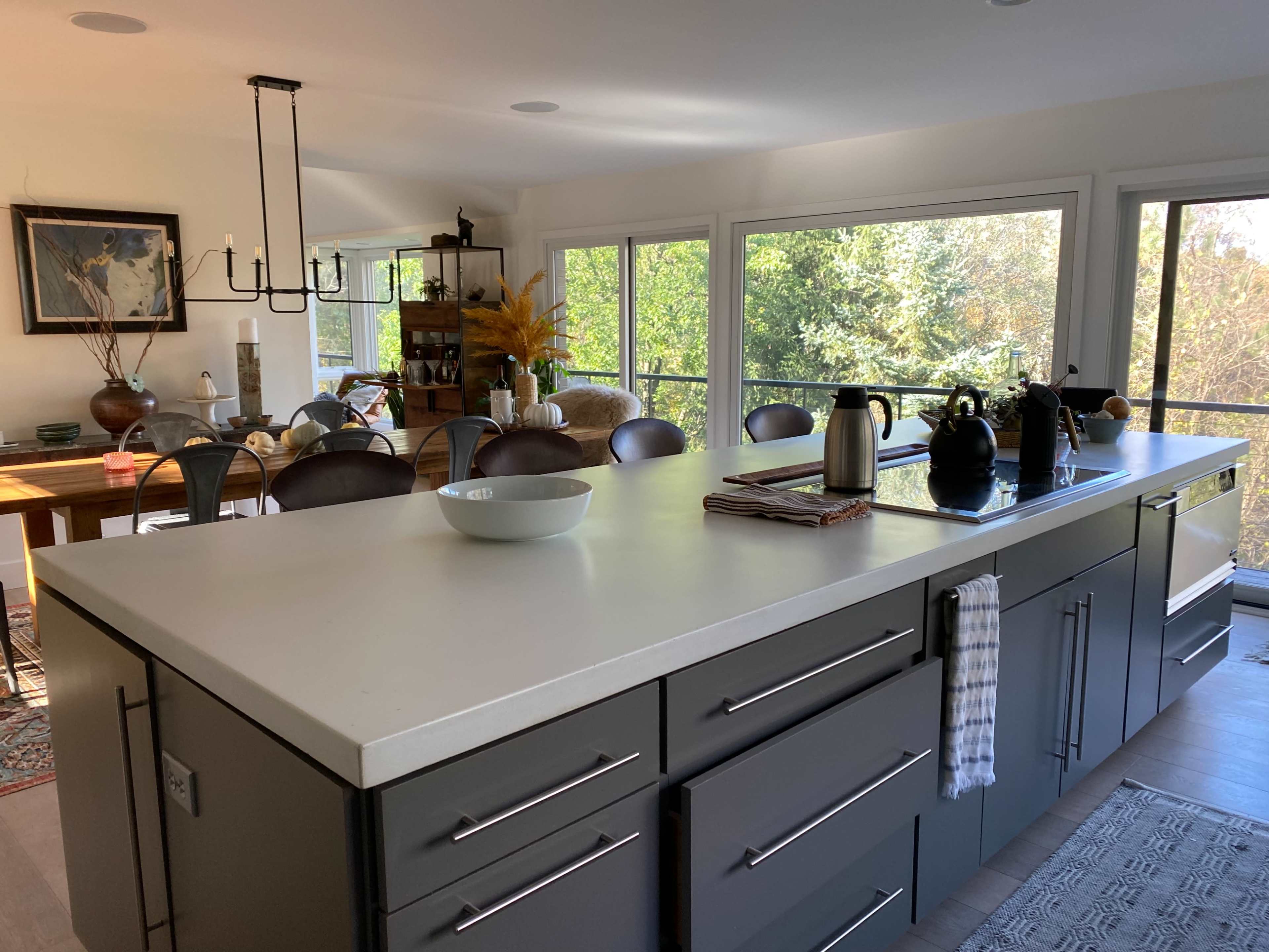 A modern kitchen with an island, gray cabinetry, and large windows overlooking a green landscape.