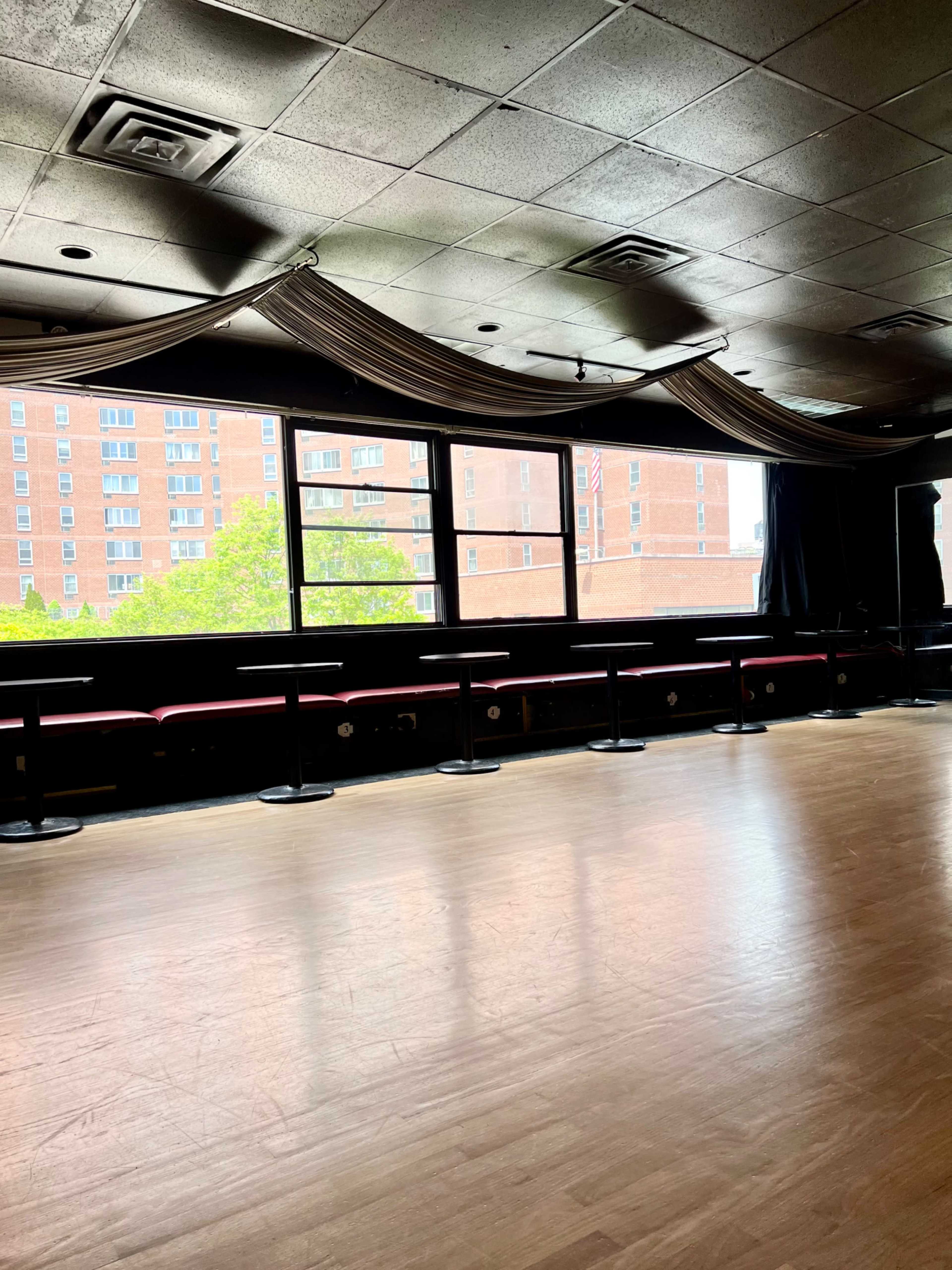 A spacious, empty dance floor with a row of seating along large windows that overlook an urban landscape.