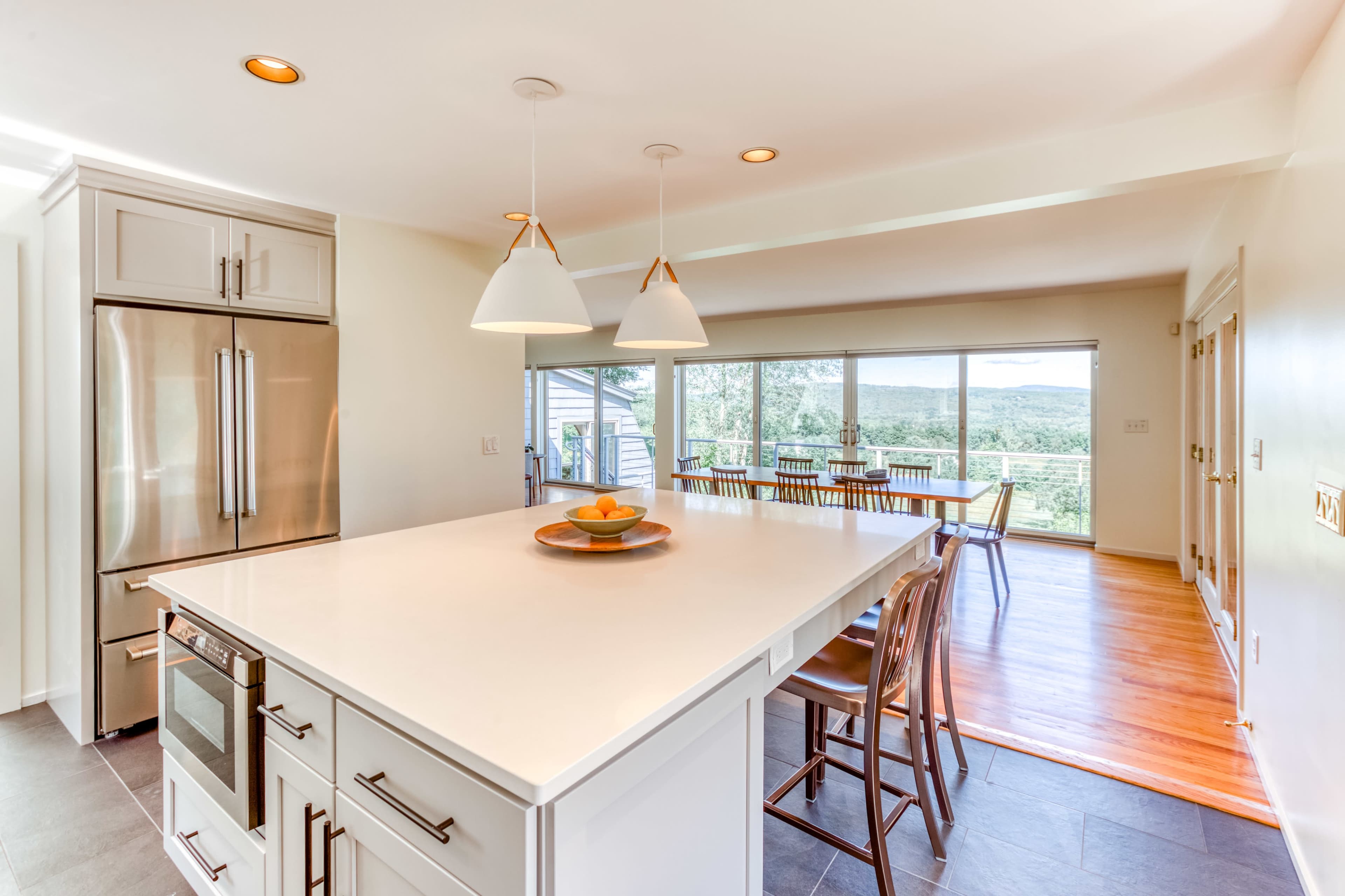 A modern kitchen features a large island with seating, stainless steel appliances, and floor-to-ceiling windows offering a view of the landscape.