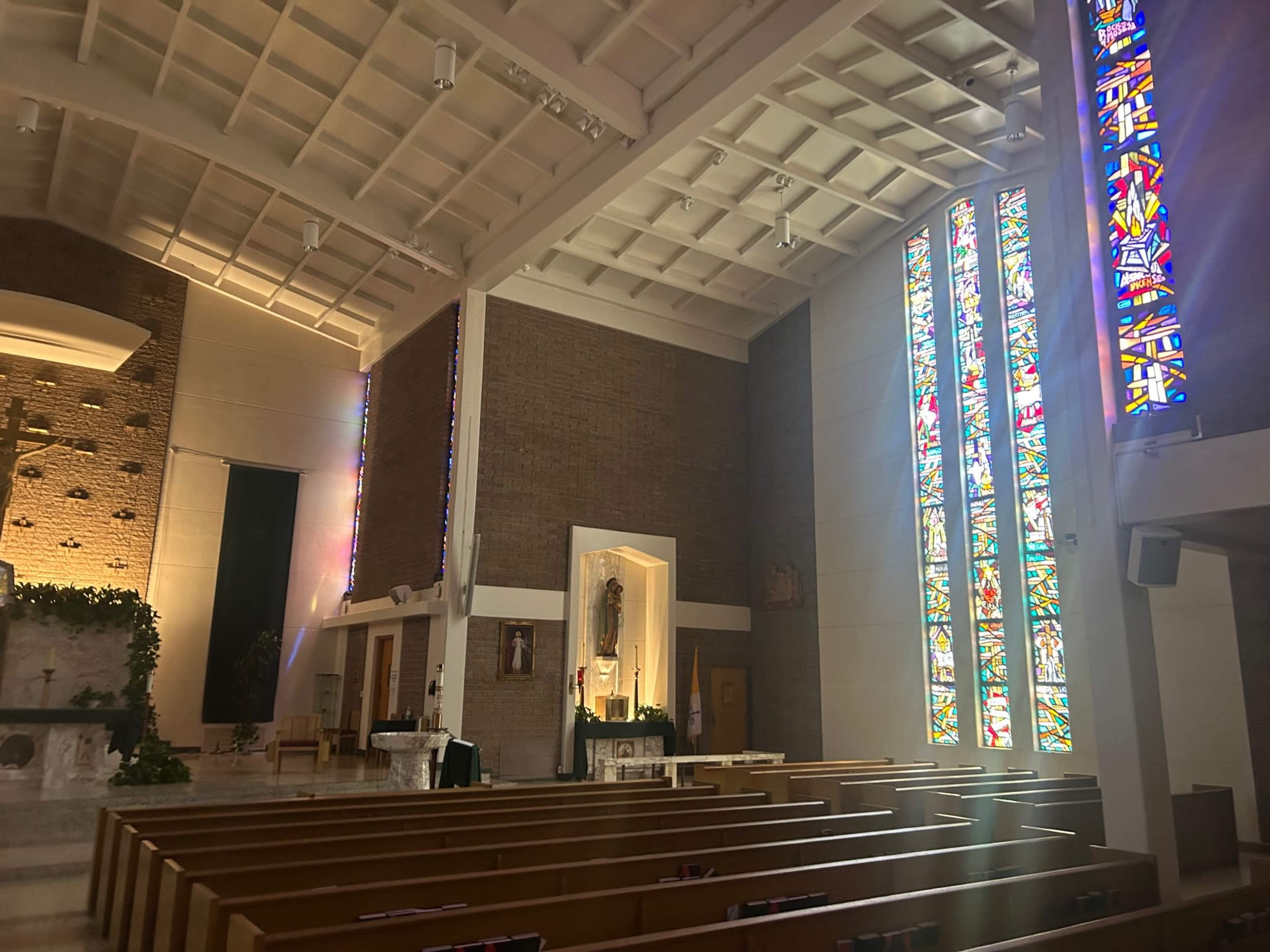 The interior of a church features wooden pews, a altar area, and large stained glass windows illuminating the space.
