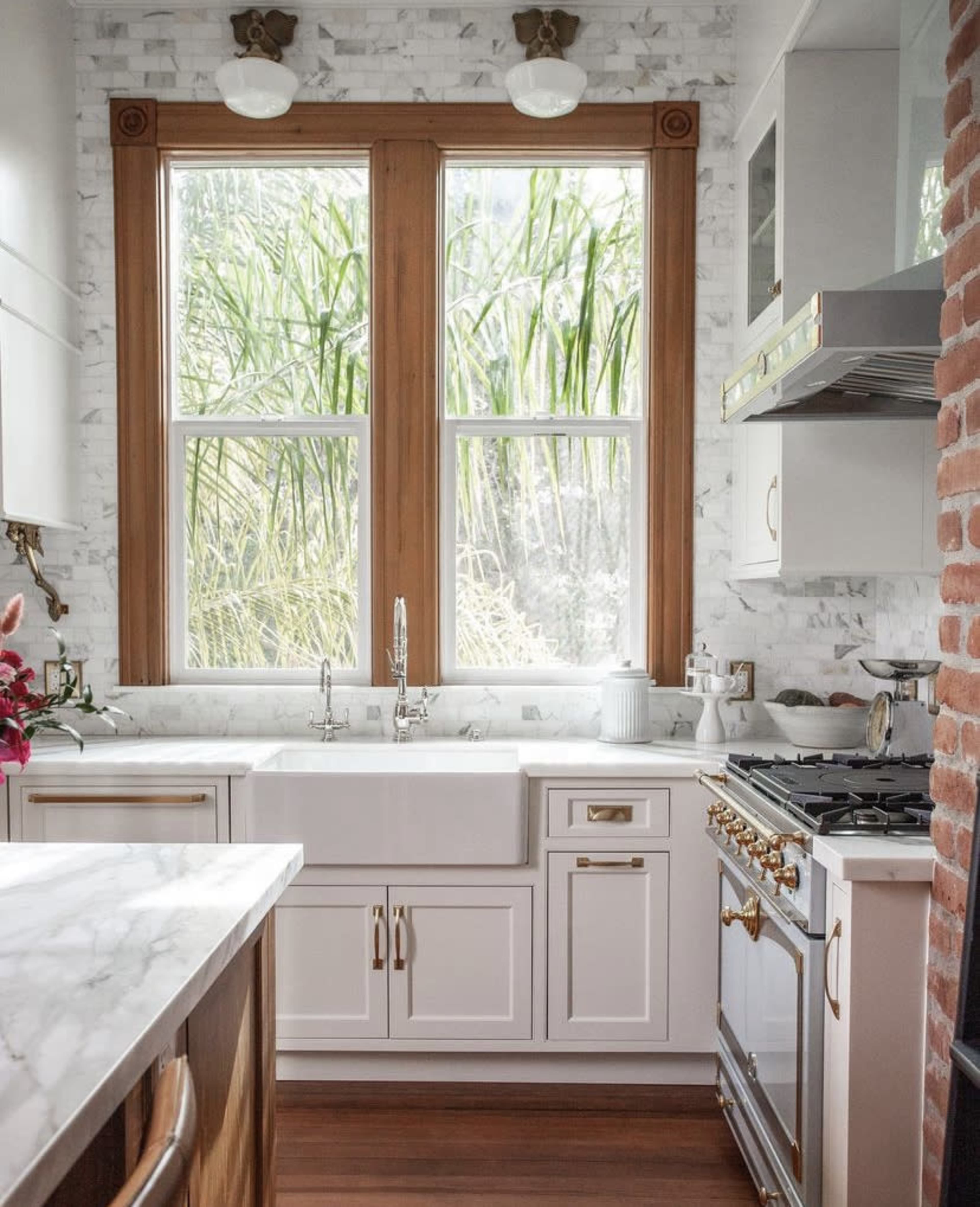 The kitchen features a white farmhouse sink, a gas stove, and large windows that overlook greenery outside.