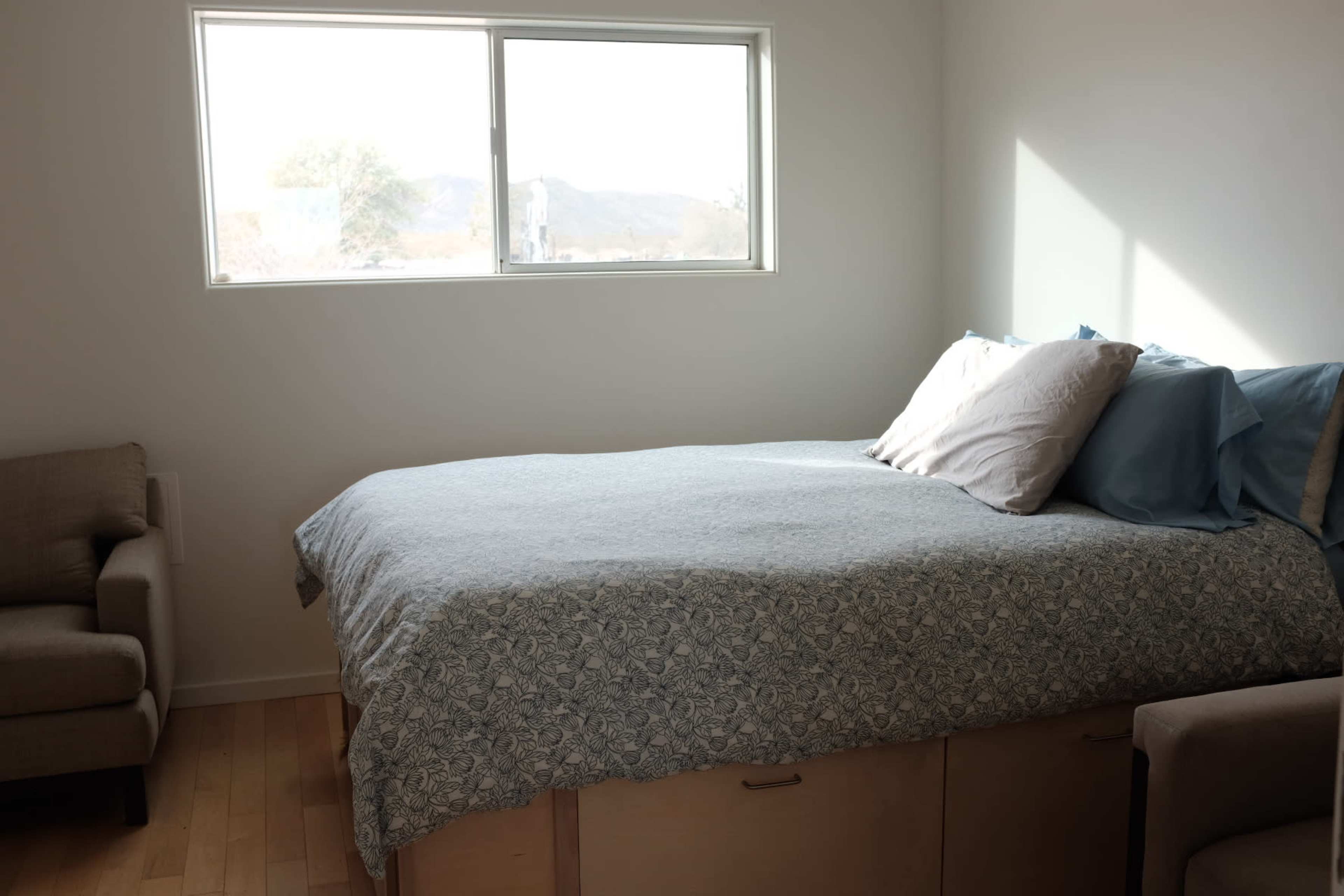 A neatly made bed with decorative pillows is positioned next to a window, allowing natural light to illuminate the room.