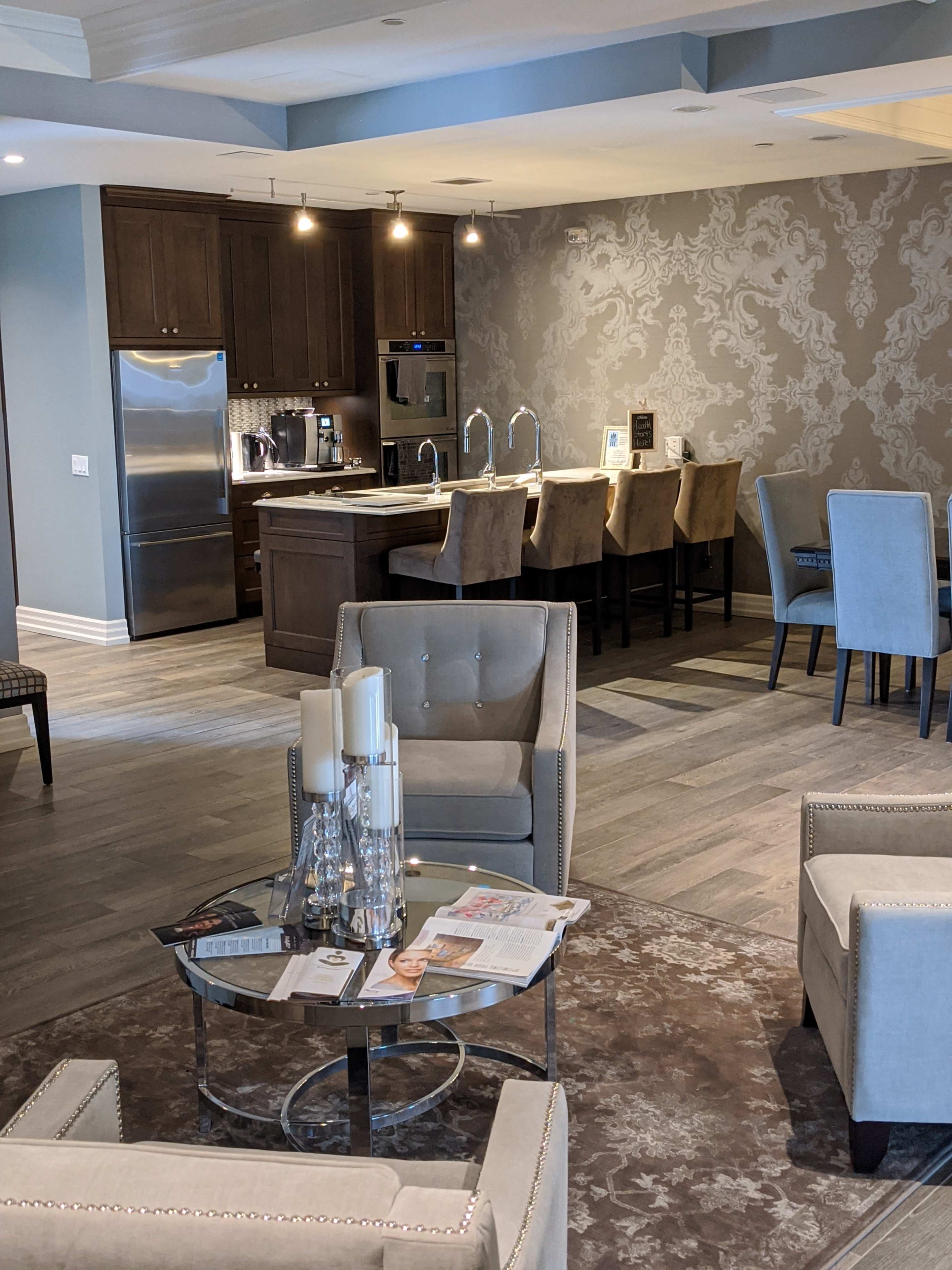 A modern, open-concept living space featuring a seating area with two armchairs, a glass table with magazines, and a kitchen island with bar stools in the background.